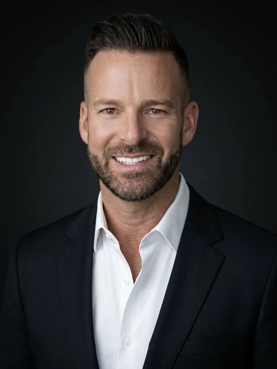 Guy Yarkoni, The Orlando Real Estate Guy, wearing a black suit and white shirt against a dark background.