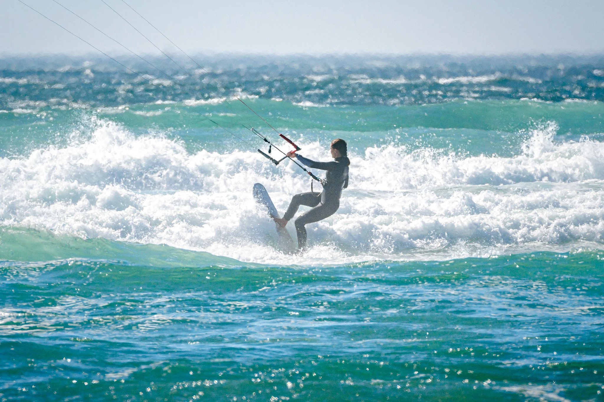 A person in a wetsuit kitesurfing on ocean waves with a kite in the sky.