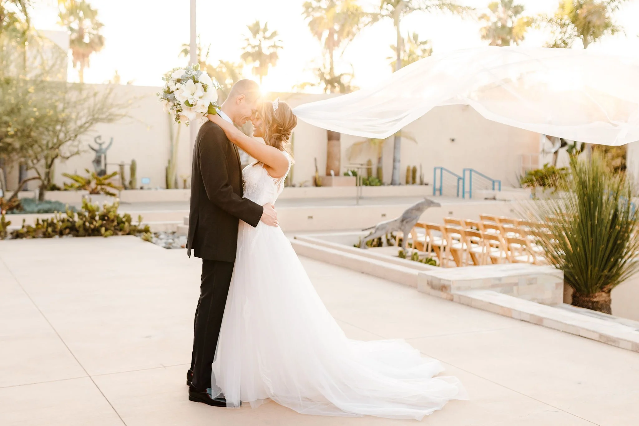 Bride and groom embracing at sunset during their wedding outside, with empty chairs and outdoor decor in background.