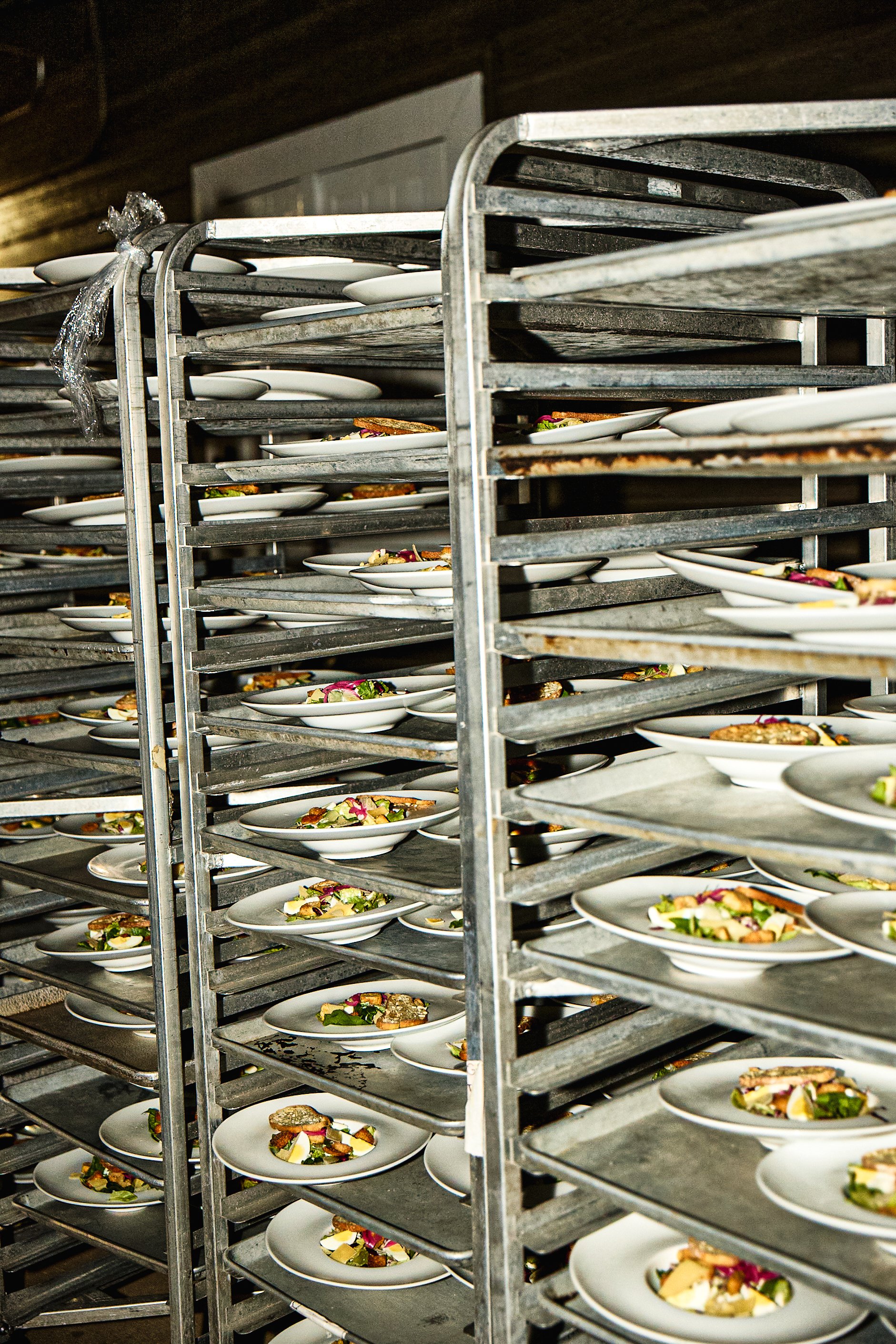 Multiple empty hotel or restaurant stainless steel racks filled with white plates of salads and appetizers.