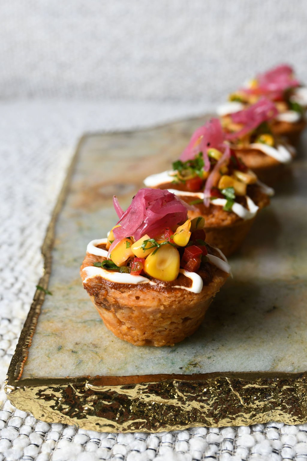 Line of mini taco appetizers topped with pickled onions, corn, salsa, and sauces on a decorative tray, done by best catering in Long Beach, TGIS Catering