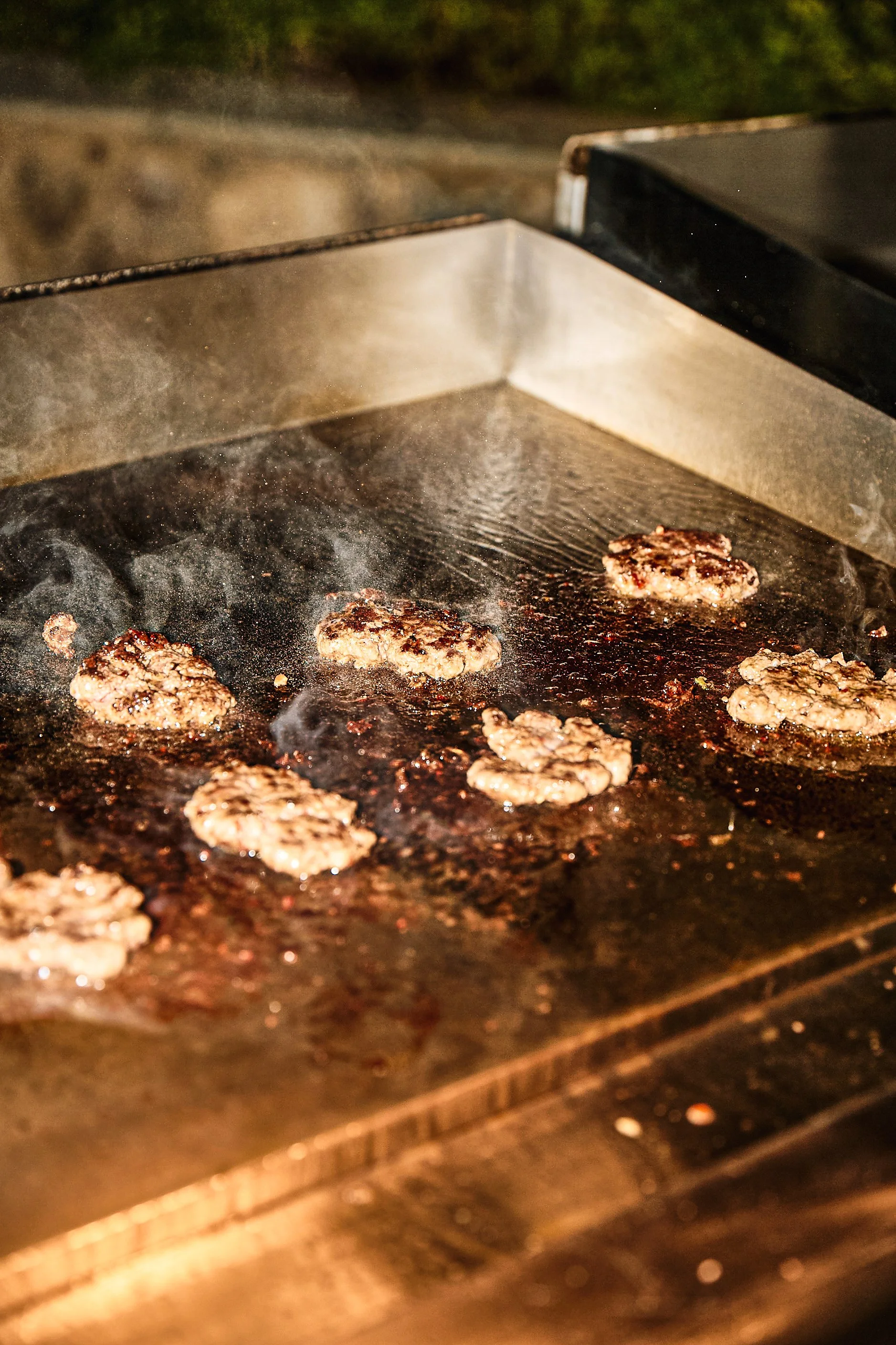 Meat patties sizzling on a flat top grill.