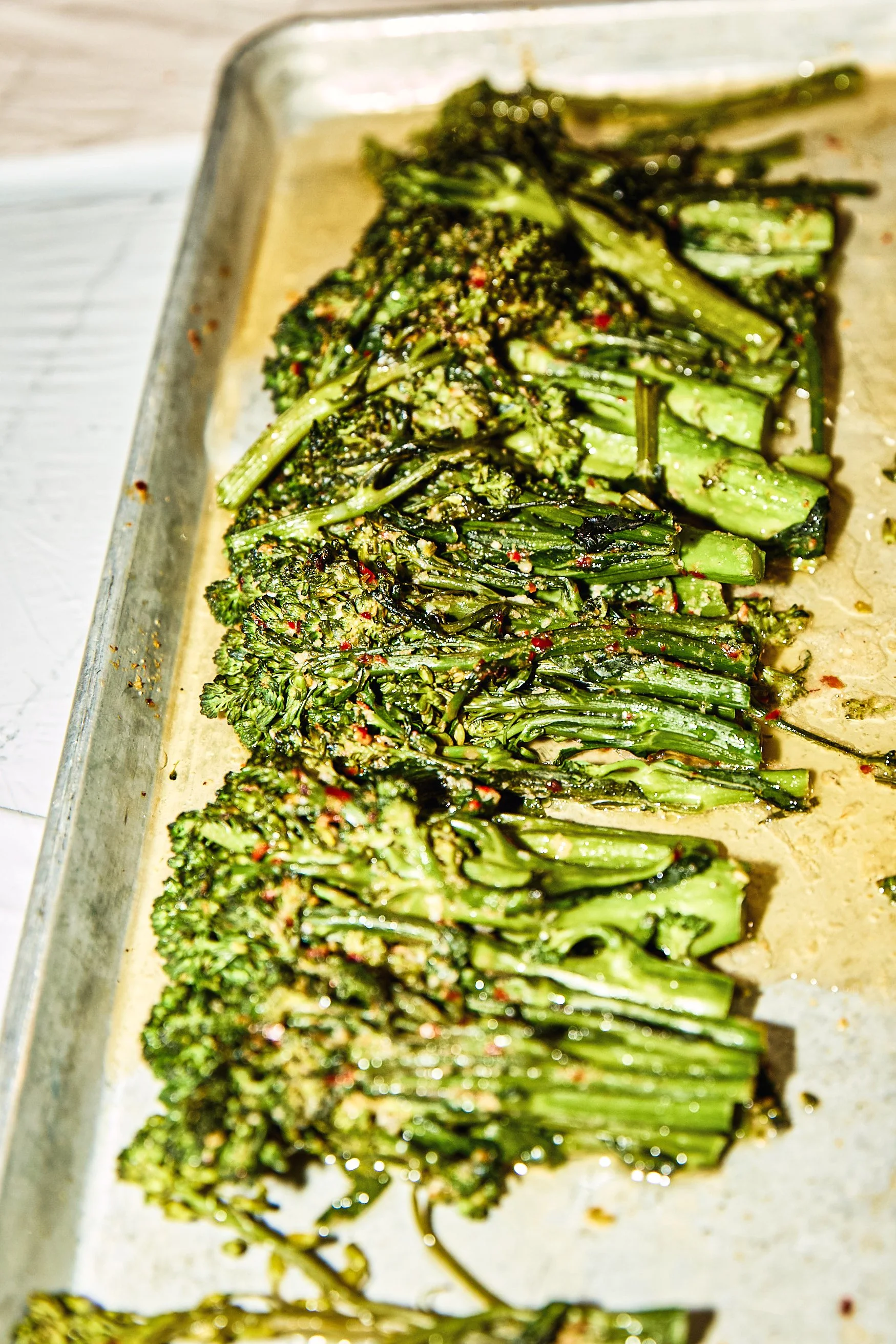 Roasted broccoli spears on a baking tray seasoned with herbs and spices.