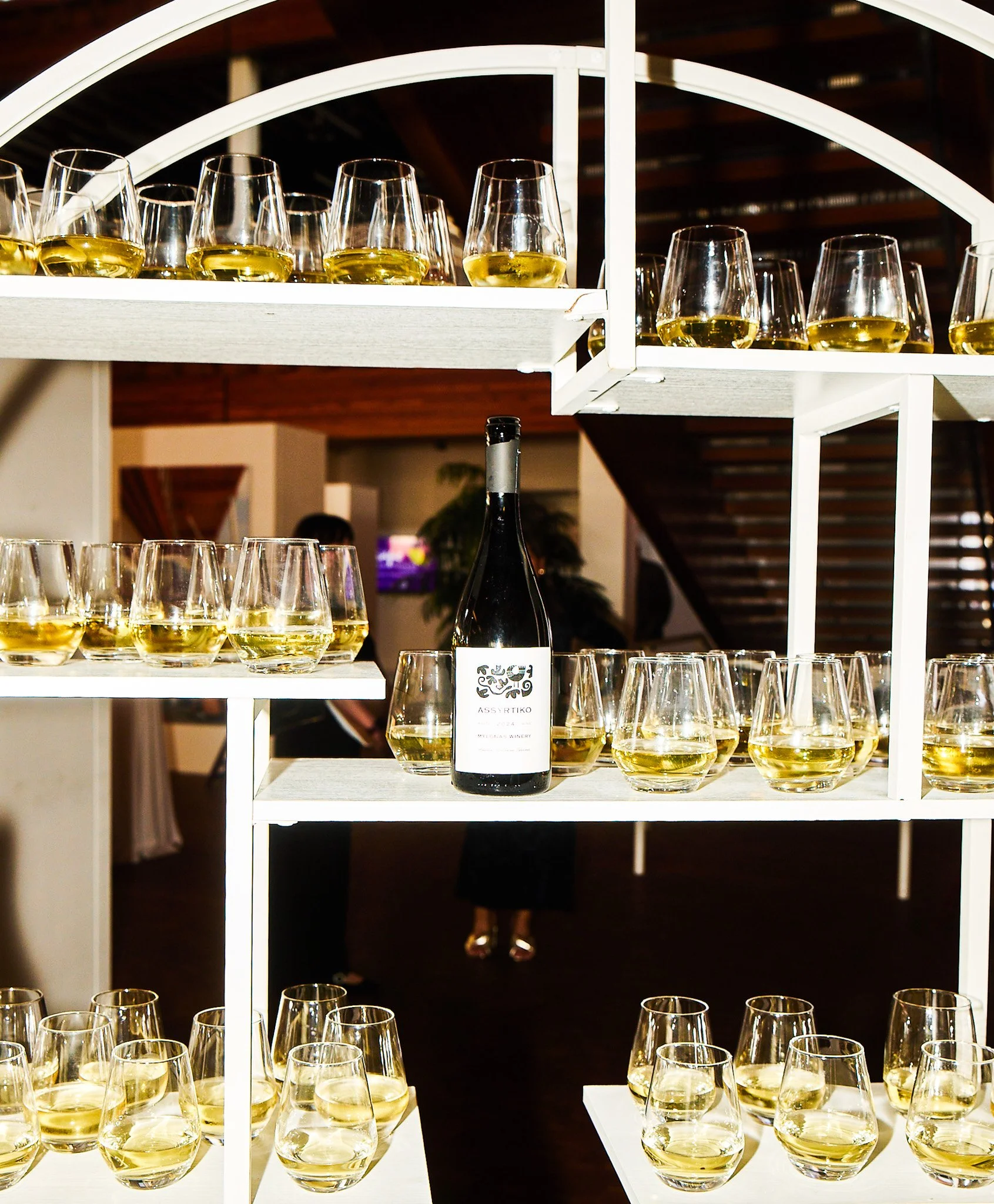 Shelf with multiple glasses of white wine and a bottle of wine in the center.