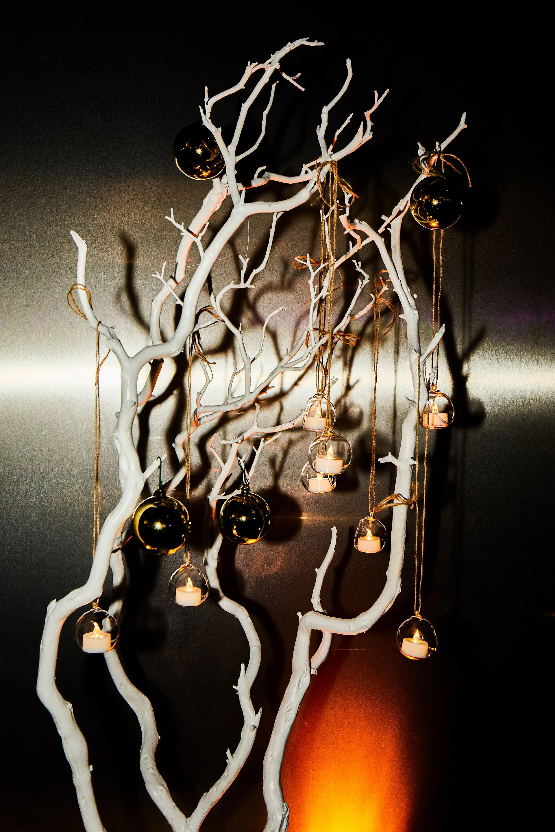 Decorative white tree branches adorned with black and gold Christmas ornaments and small candles hanging from gold strings.