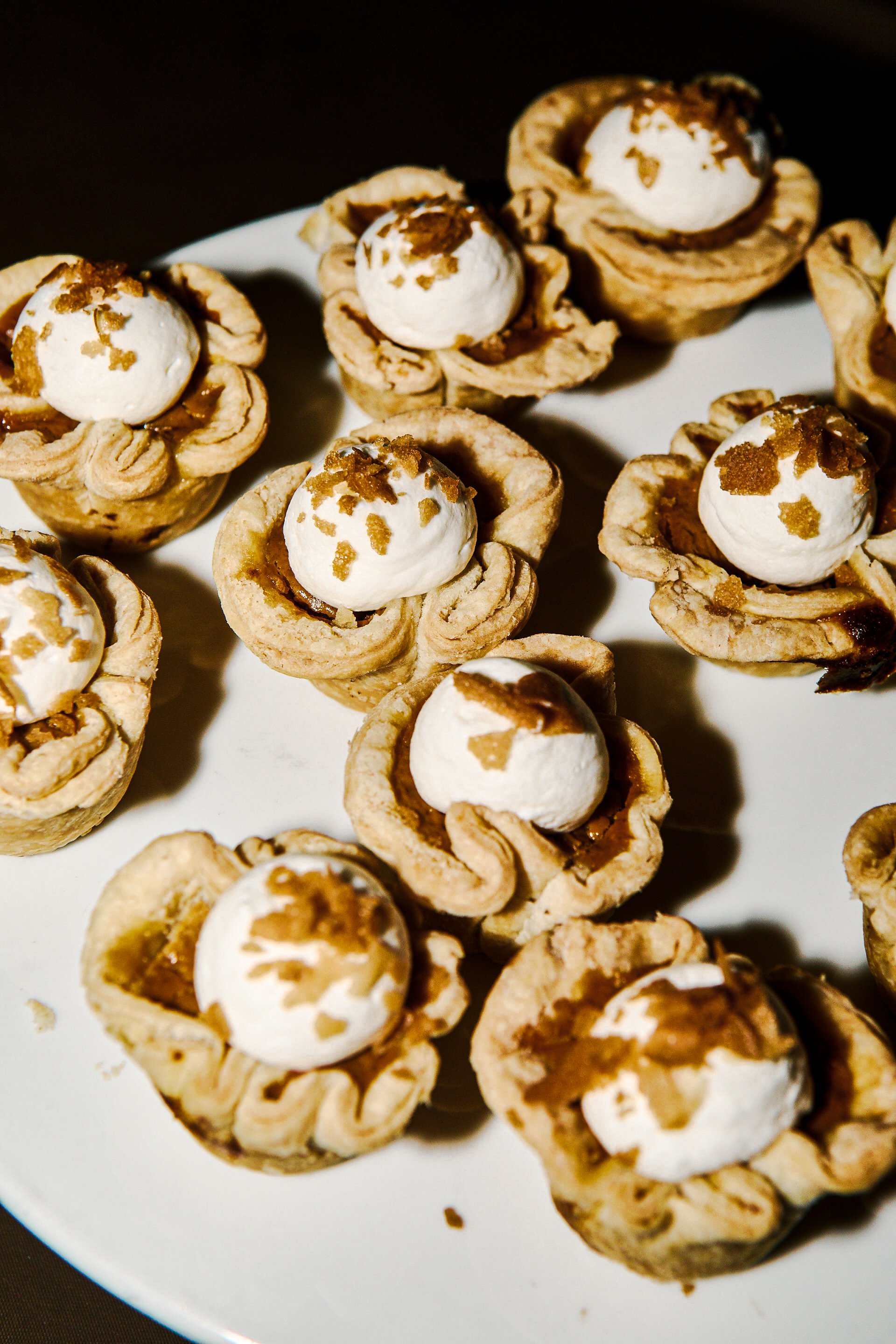 Miniature tartlets topped with whipped cream and caramelized nuts on a white plate.
