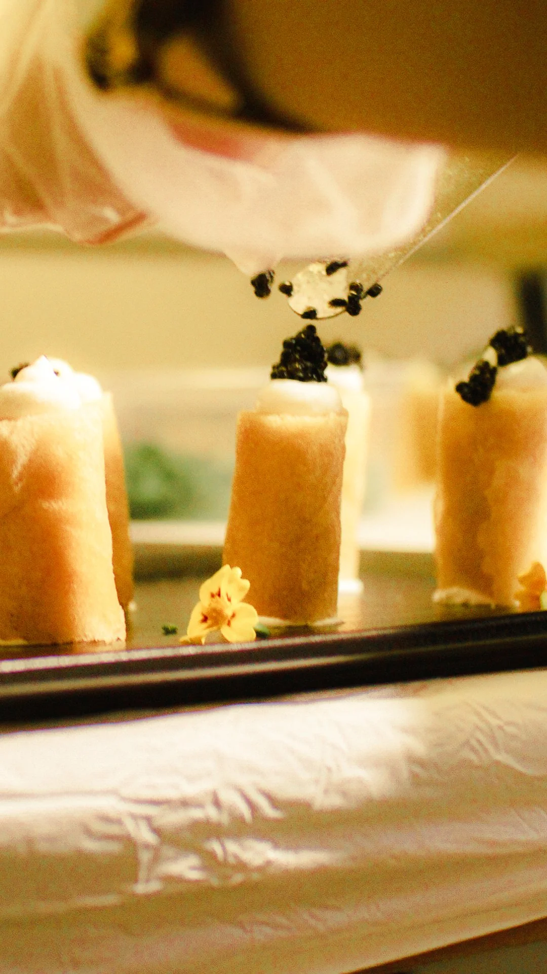 Miniature sponge cakes topped with whipped cream and small black caviar, with a decorative flower on a tray.