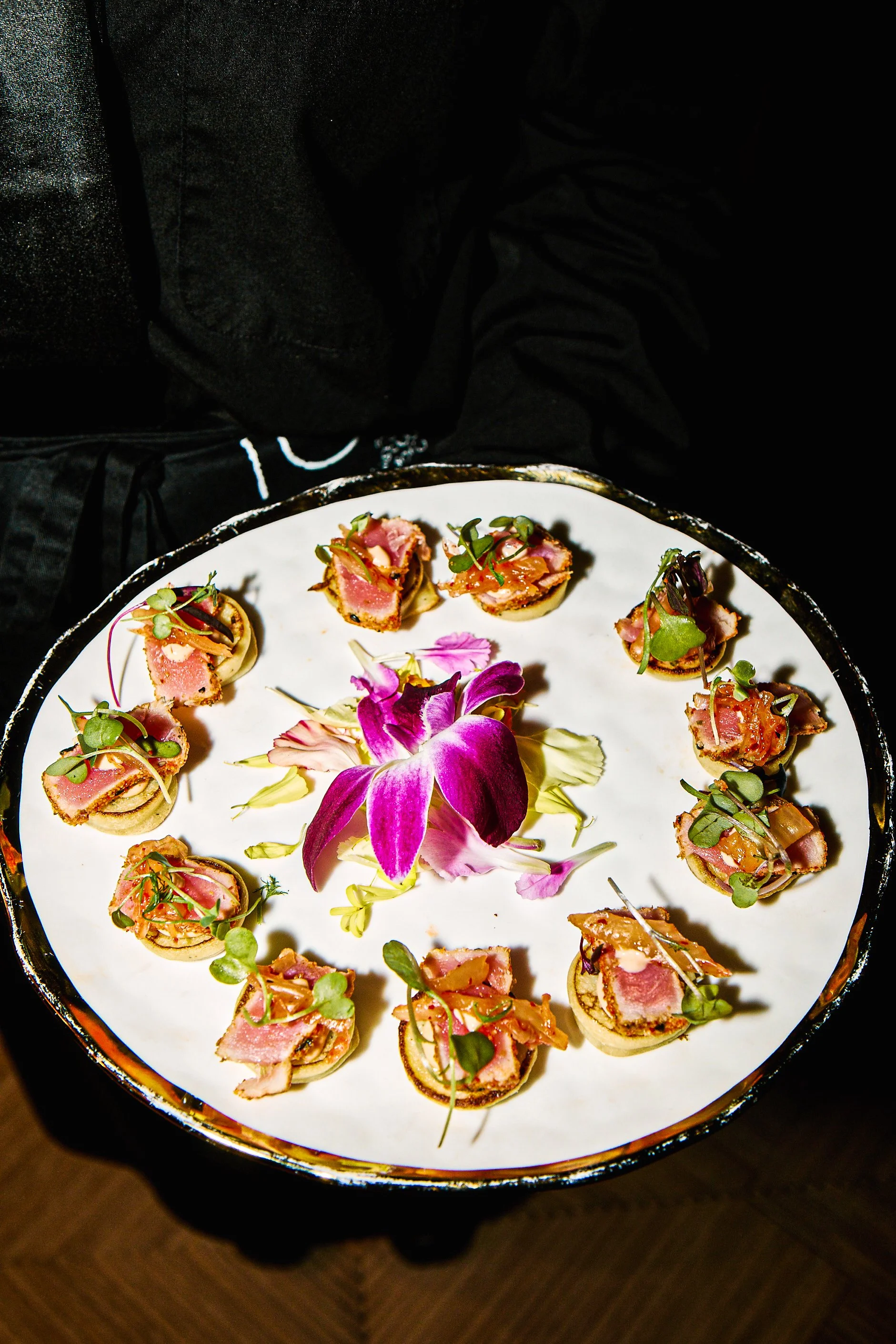A round platter with small appetizers arranged in a circle, garnished with microgreens and edible flowers in the center.