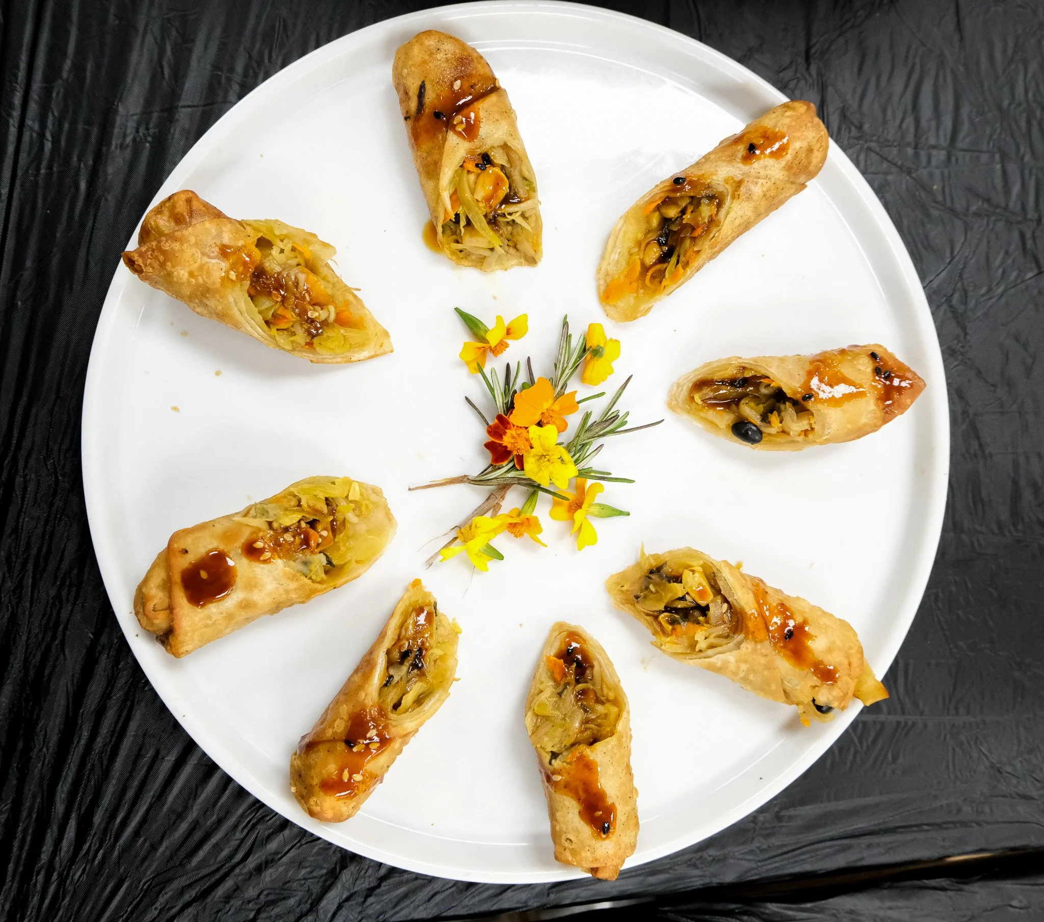 Vegetable egg rolls sitting on a white serving platter with micro flowers in the middle for presentation 