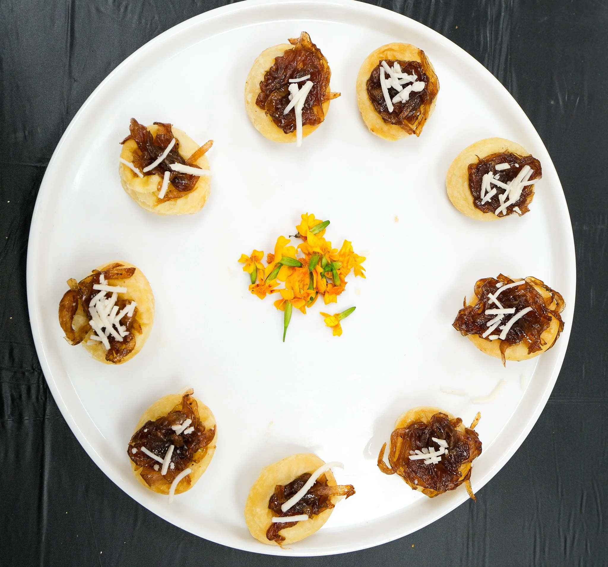 Baked appetizer sitting on a white serving platter with micro flowers in the middle for presentation