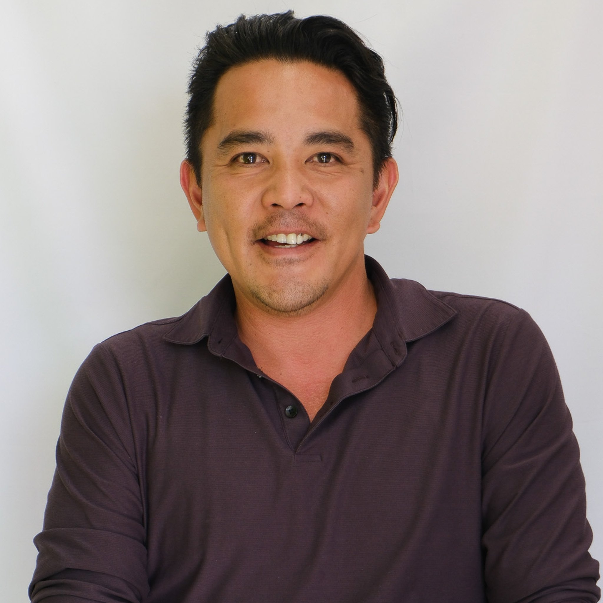 Professional headshot of a smiling man in a navy blazer and white shirt against a gray background.