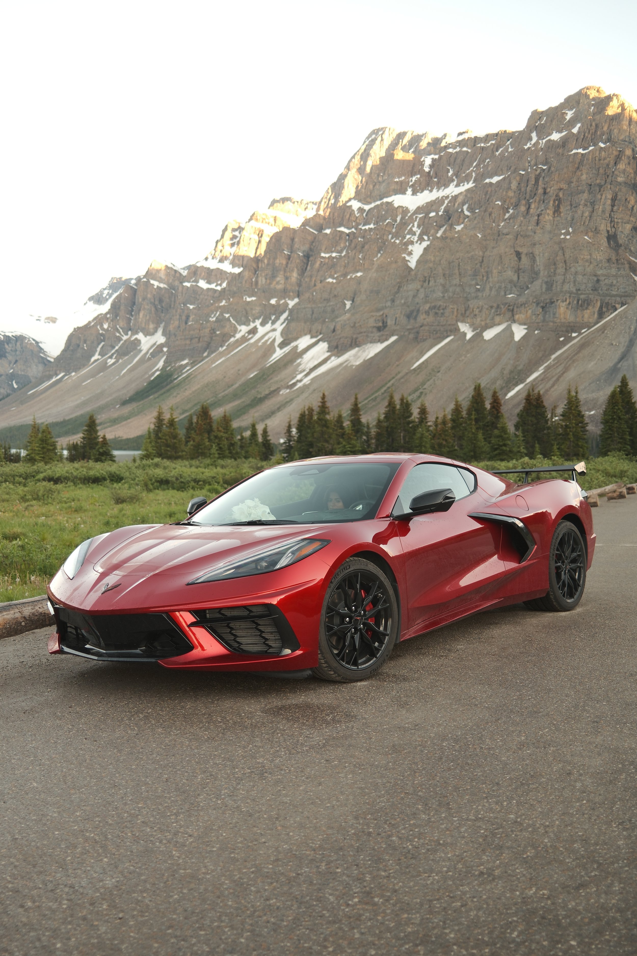 Red sports car parked on the side of a road with mountains and trees in the background