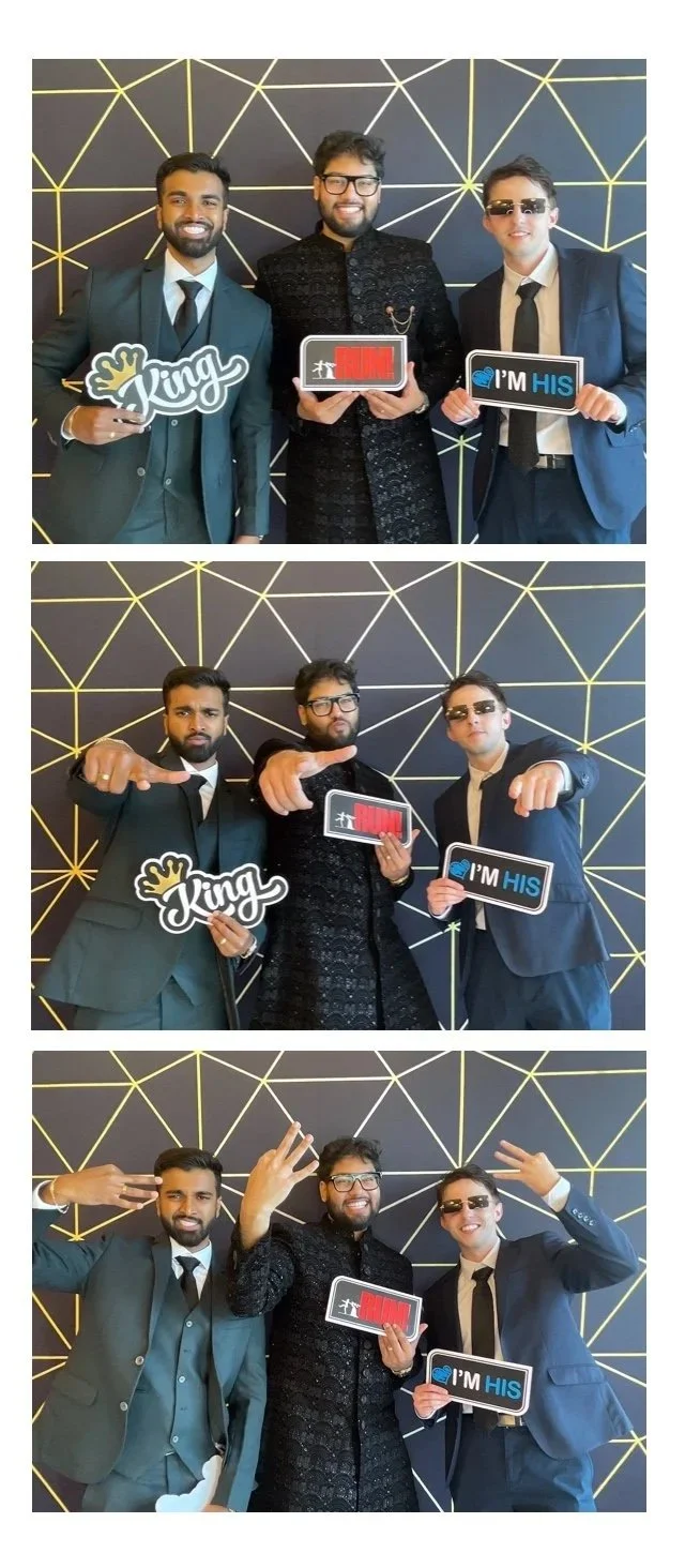 Three men in formal suits and sunglasses, holding signs that say "King," "Run," and "I'M HIS," posing in front of a black and gold geometrical patterned background. The trio is making various hand gestures in a photo booth style.