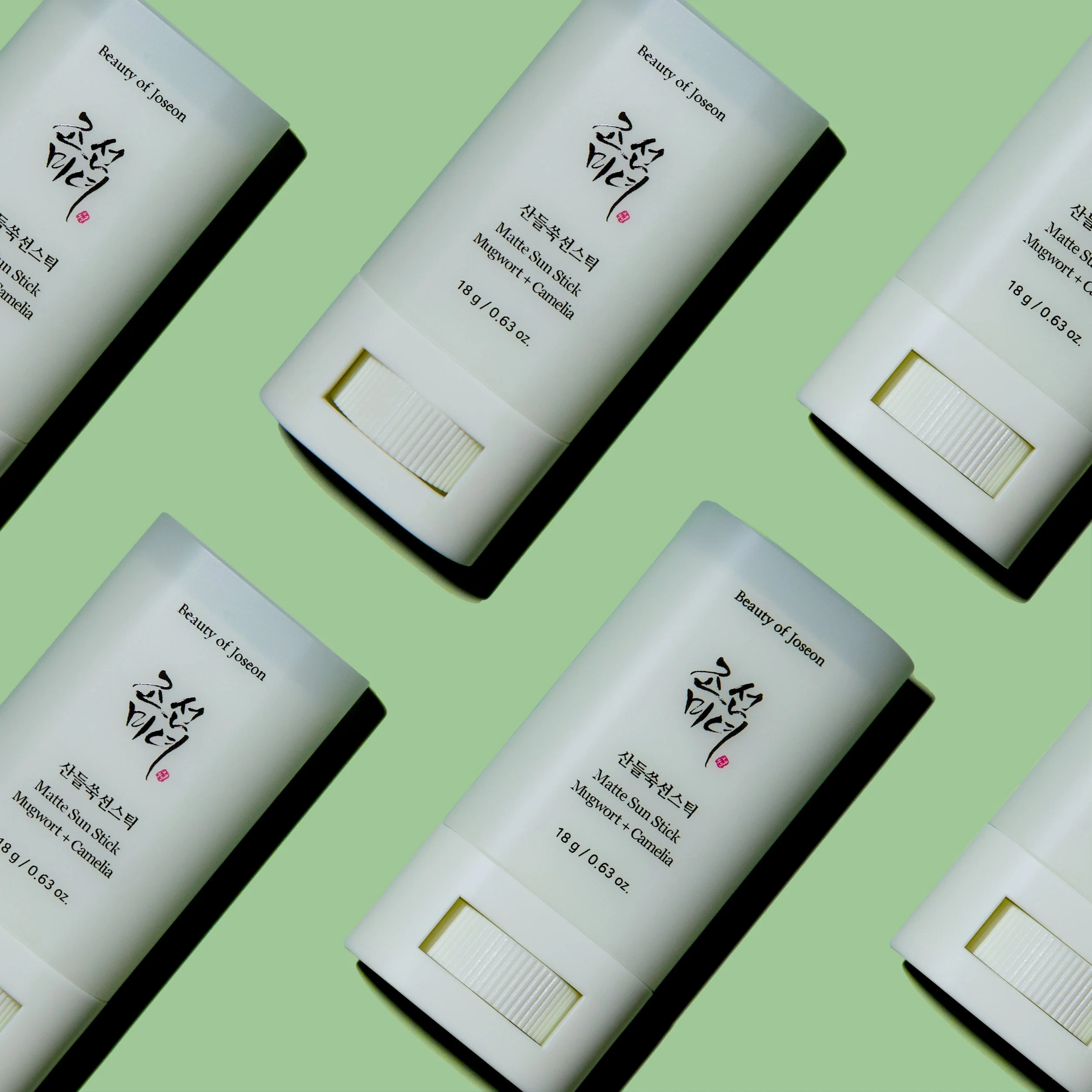 Multiple Beauty of Joseon pale green sunscreen sticks, labeled in Korean and English, on a bright green background.