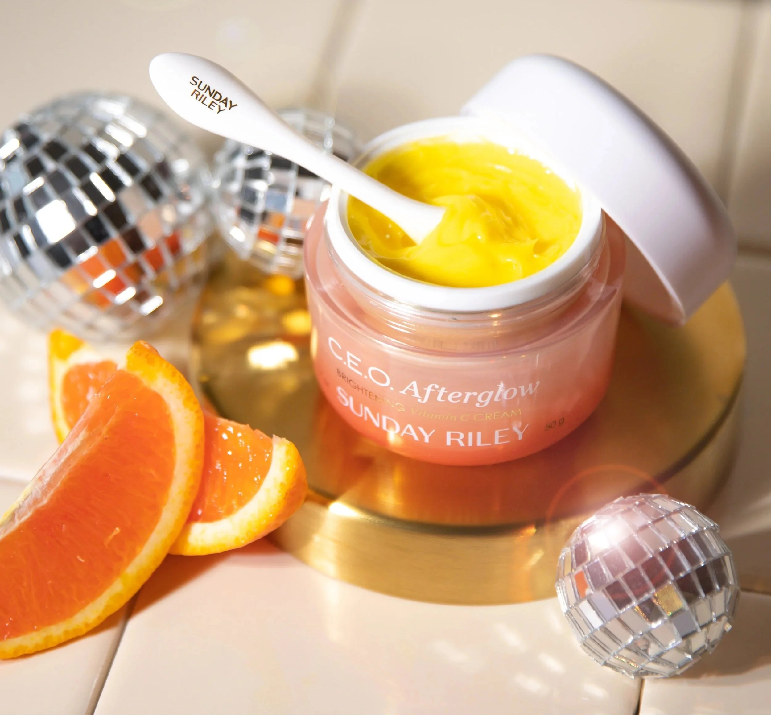 Colorful container of Sunday Riley Vitamin C cream with orange slices and disco ball decorations around it.