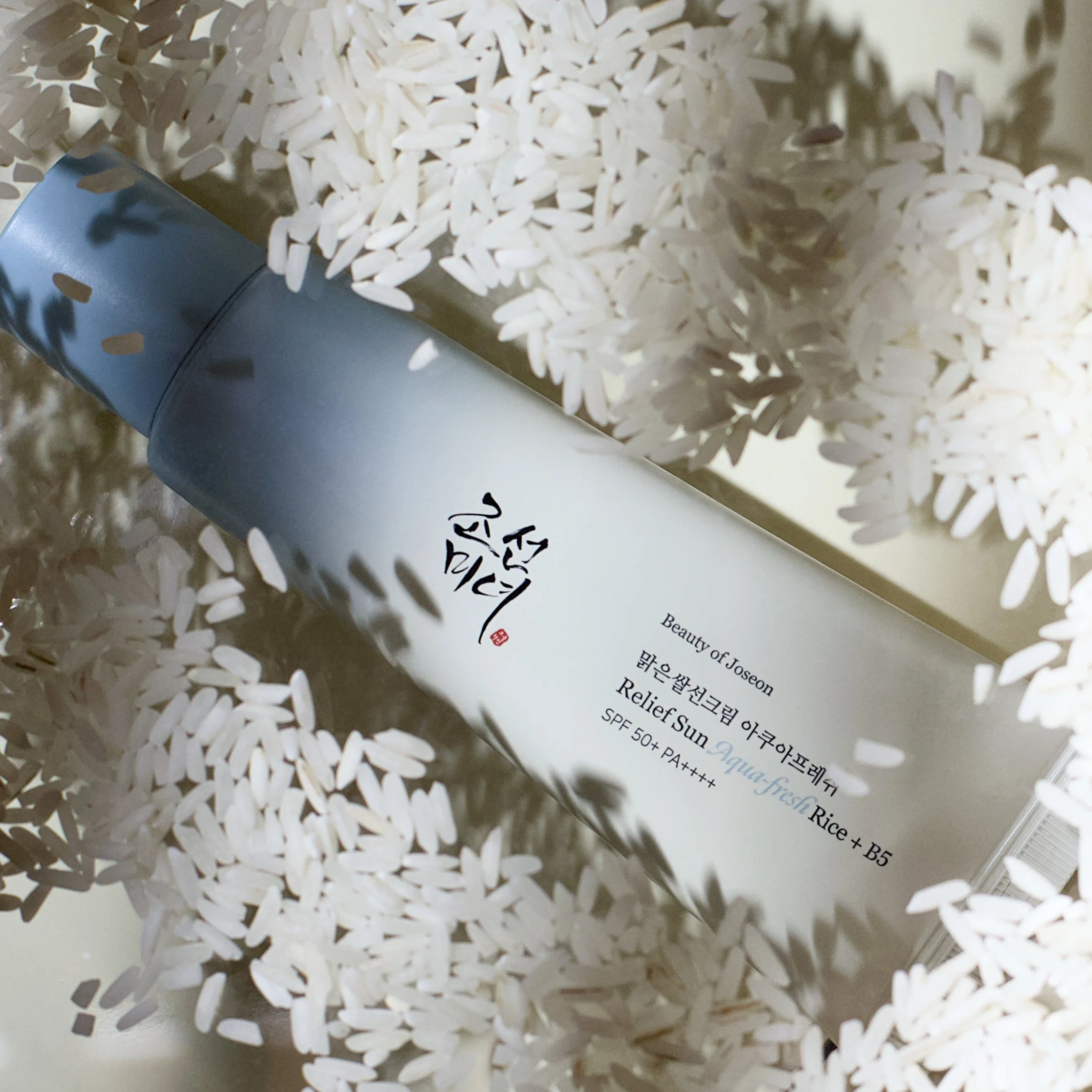 Close-up of a Beauty of Joseon sunscreen container with Korean and English text, surrounded by a large amount of white rice grains.