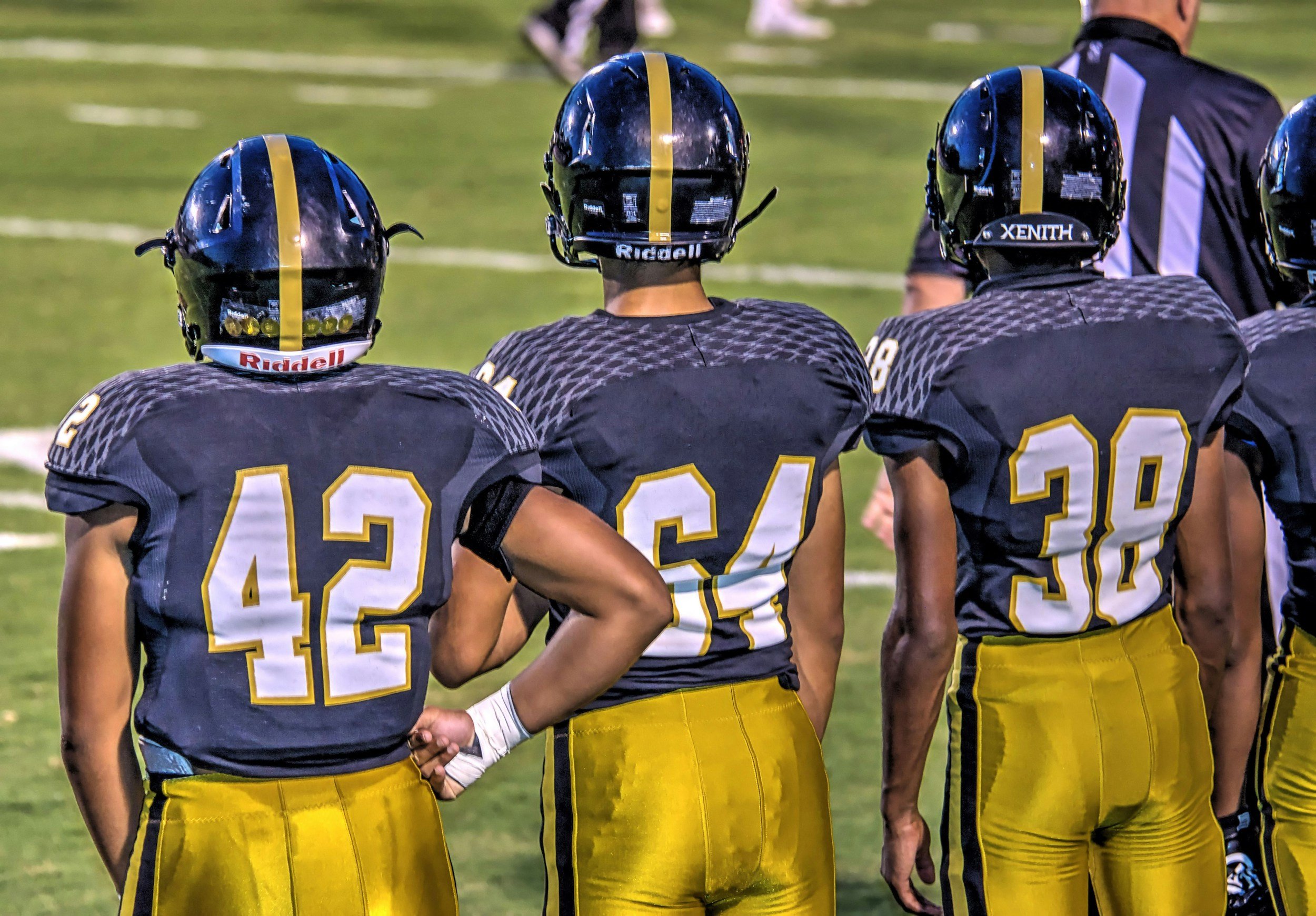 A group of football players with black helmets and yellow jerseys standing on the field during a game.