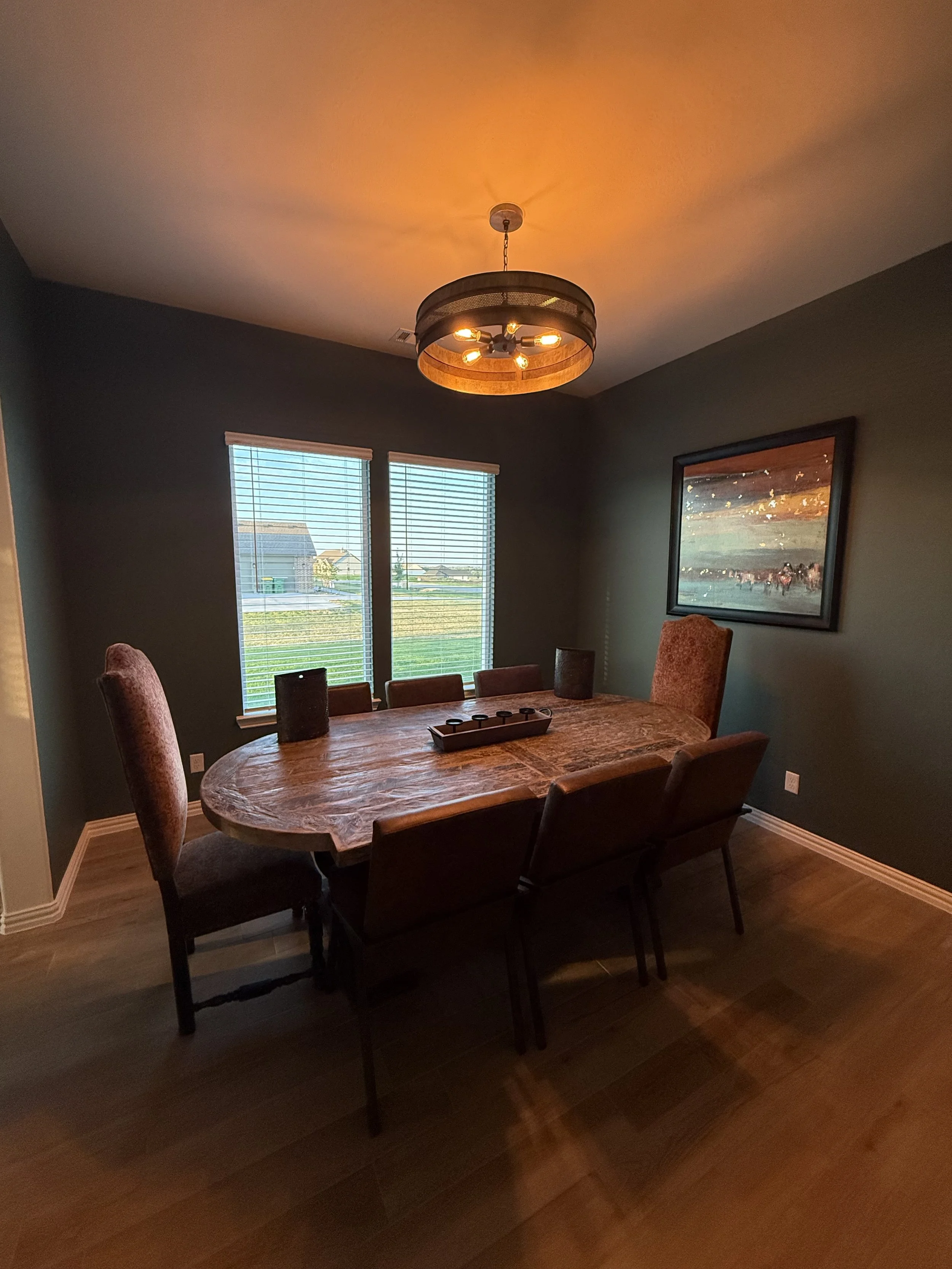 Dining room with dark green accent walls and a wagon-wheel style chandelier over a live-edge table, interior finish work by MZL Construction in Dallas-Fort Worth
