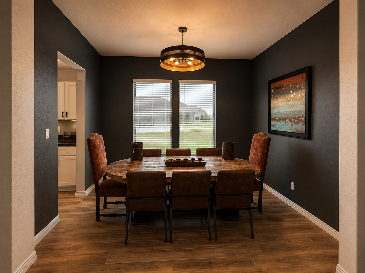 Dining room with a wooden table and six chairs, two tall brown chairs and four shorter brown chairs, two vases and a tray on the table, dark gray walls, window with blinds, wall art, wooden flooring, ceiling light fixture.