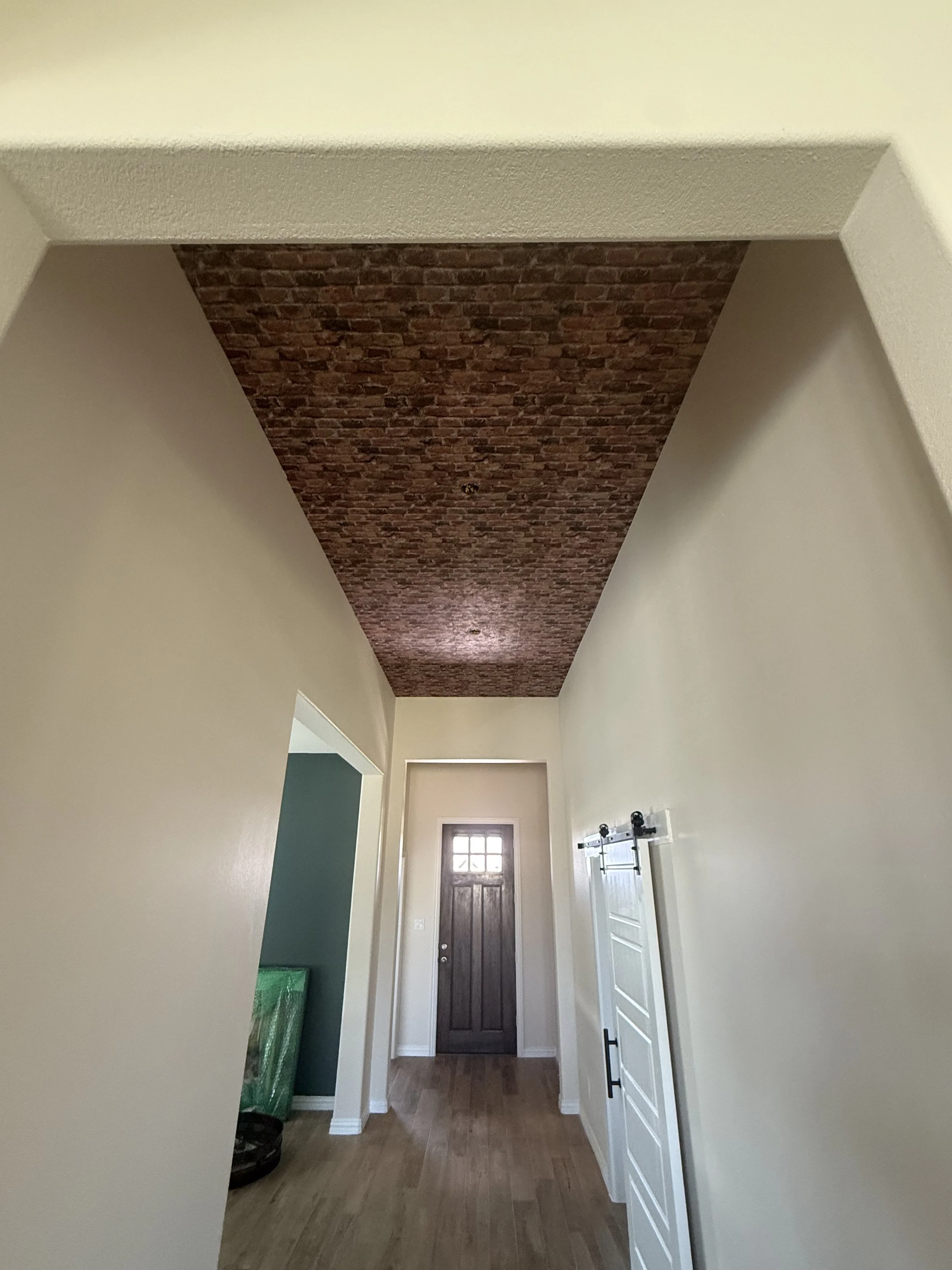 Renovated entryway hallway in a Dallas-Fort Worth home with brick-look accent ceiling, black lantern chandeliers, and sliding barn door by MZL Construction