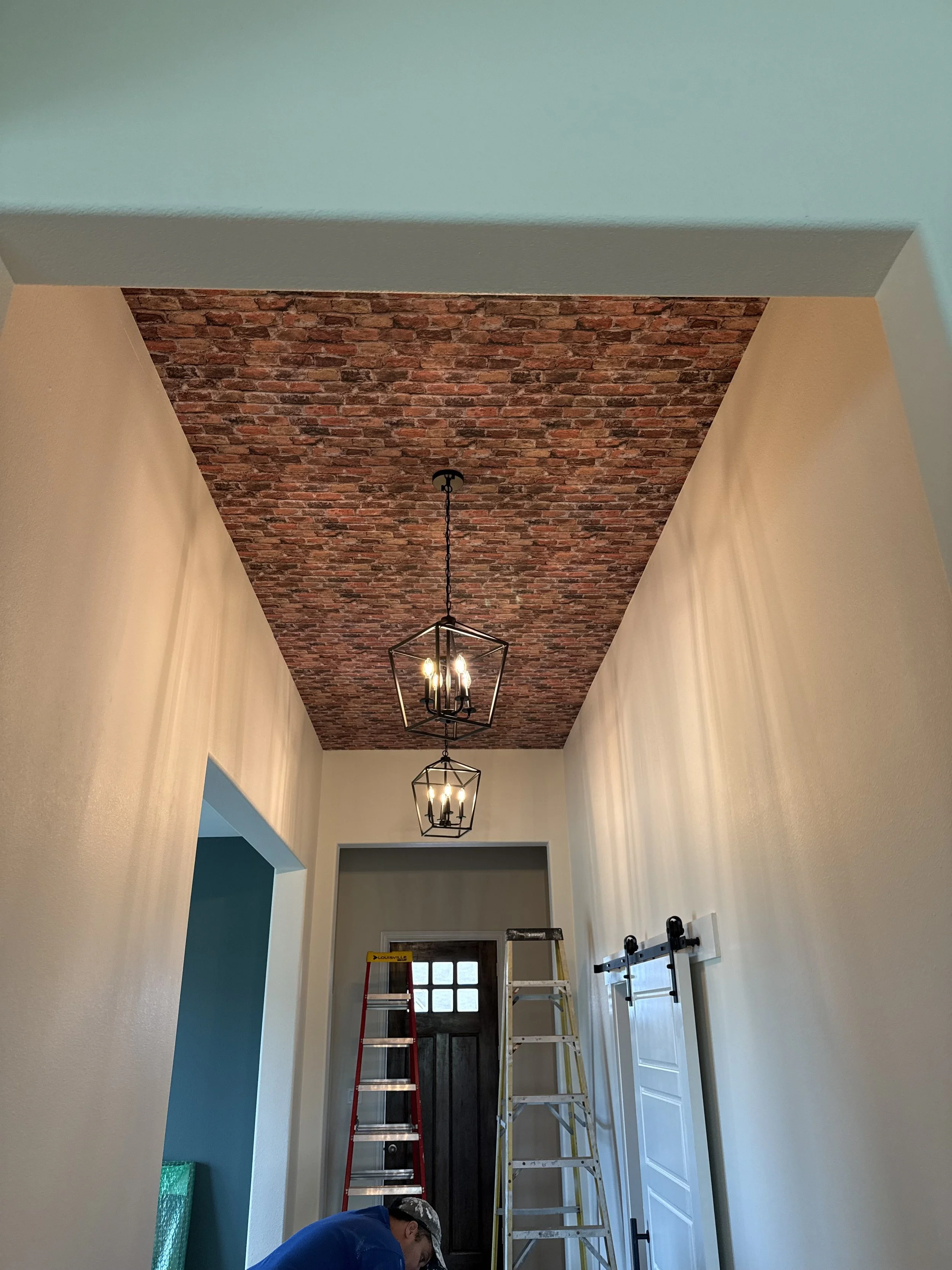 MZL Construction crew installing pendant chandeliers in a vaulted entry hallway with brick-accent ceiling and teal accent wall