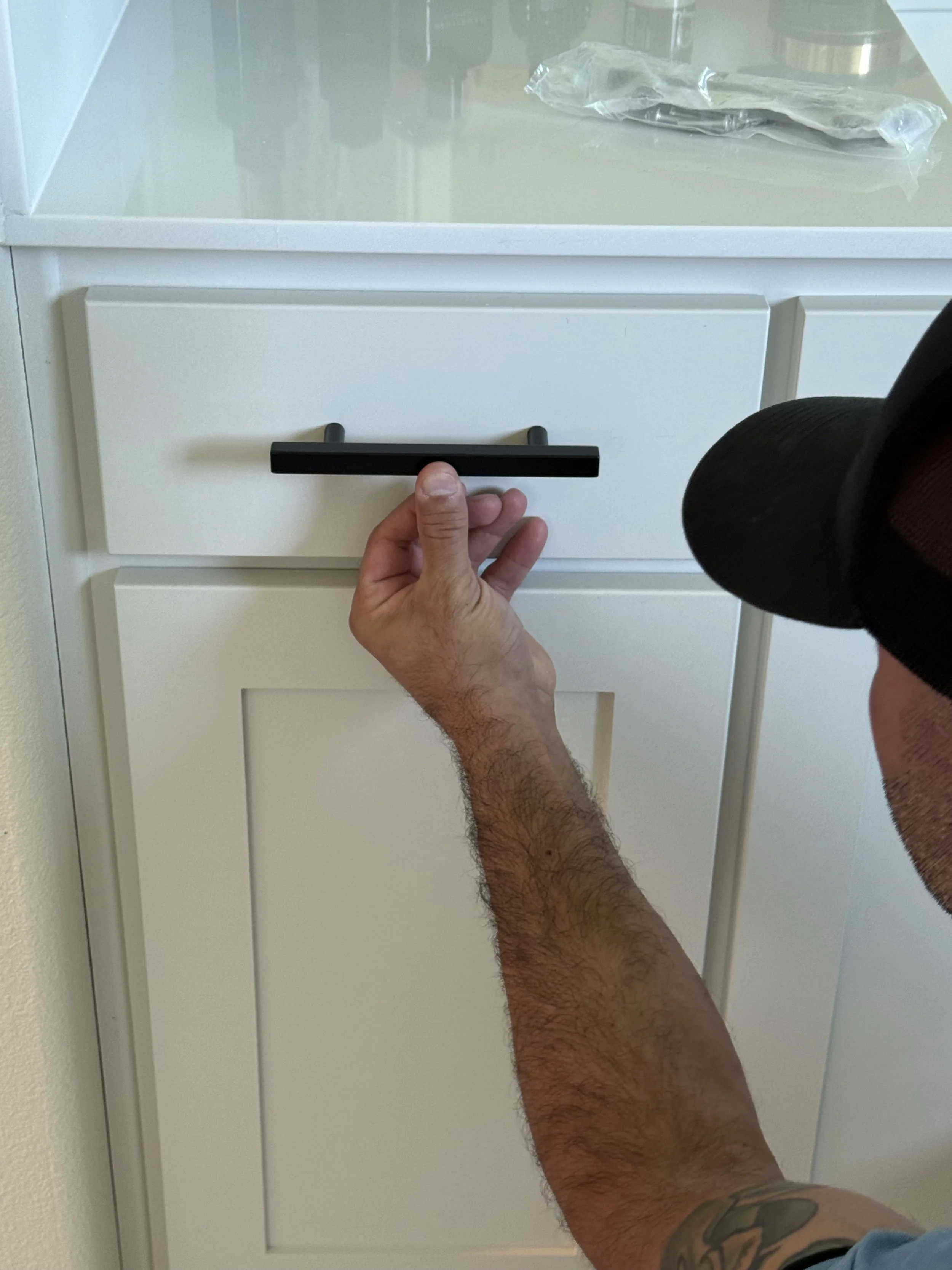 MZL Construction technician installing matte black cabinet hardware on white shaker cabinets during a Dallas-Fort Worth kitchen remodel