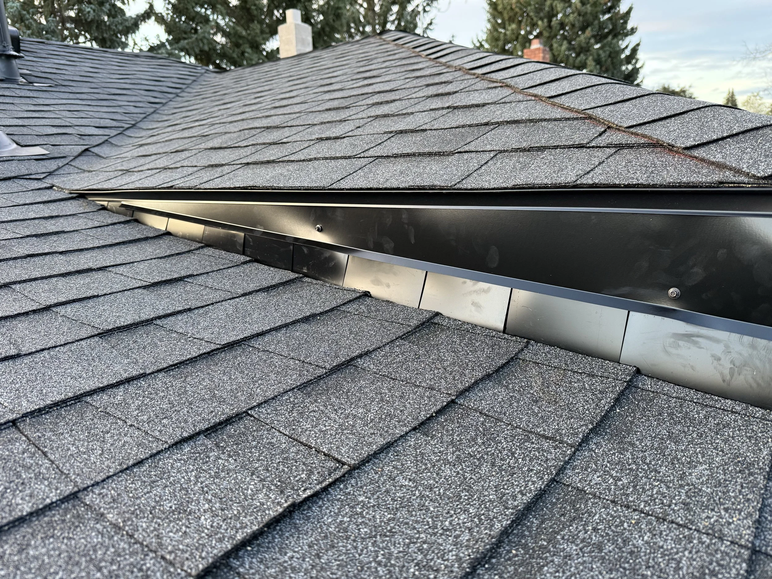 Close-up of a shingled roof with asphalt shingles and a metal vent.