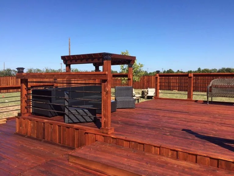 A spacious wooden deck with a privacy fence, outdoor seating, and a small shaded structure.