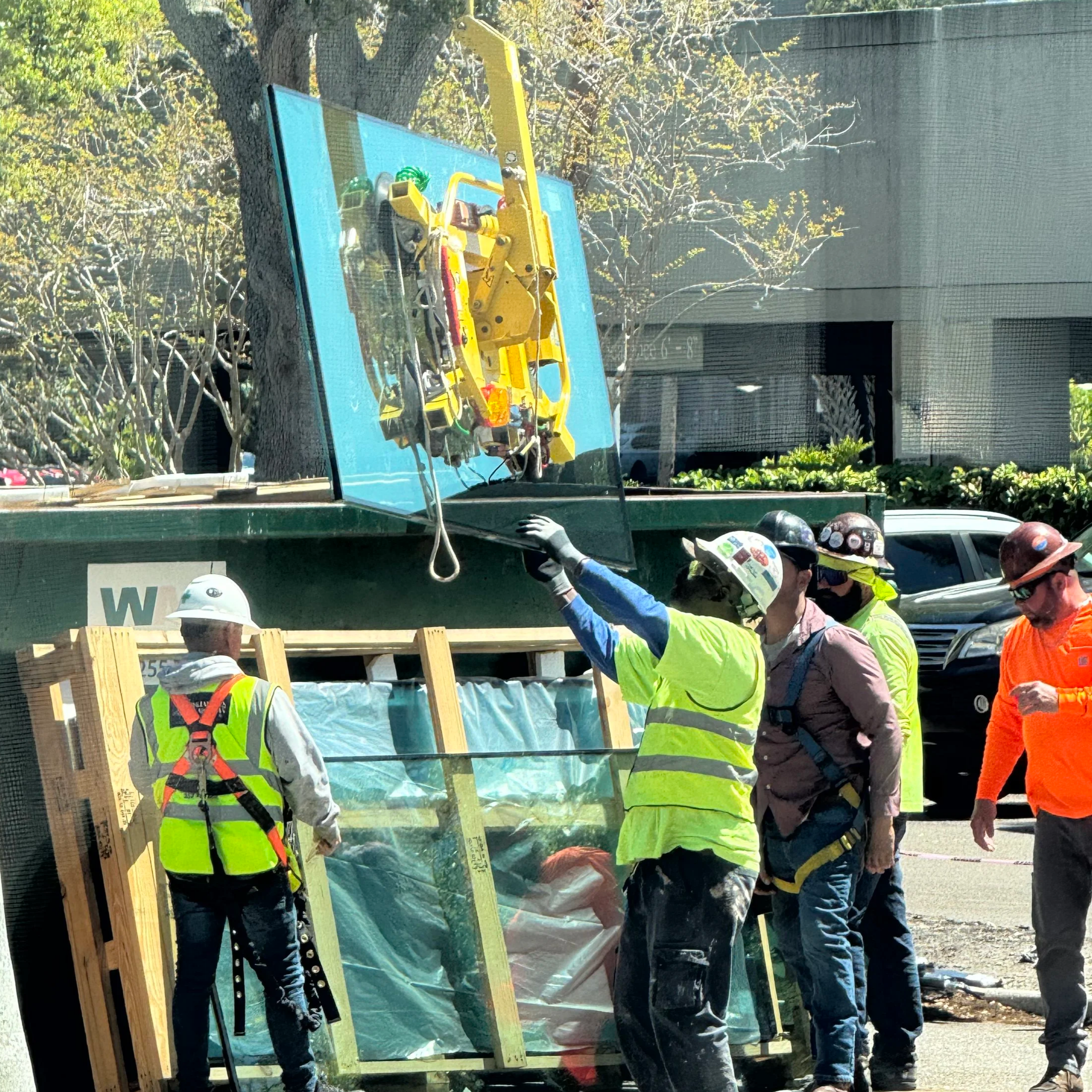 Construction workers in safety vests and helmets working on a building site, with tools and wooden framing visible, and trees in the background.