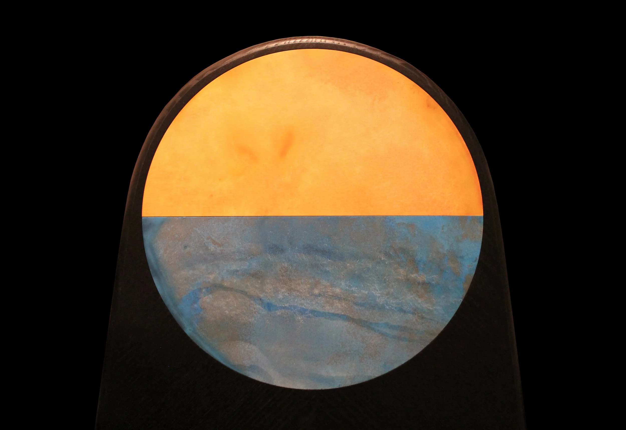A half orange, half blue, dome-shaped lamp with a black exterior on a dark background.