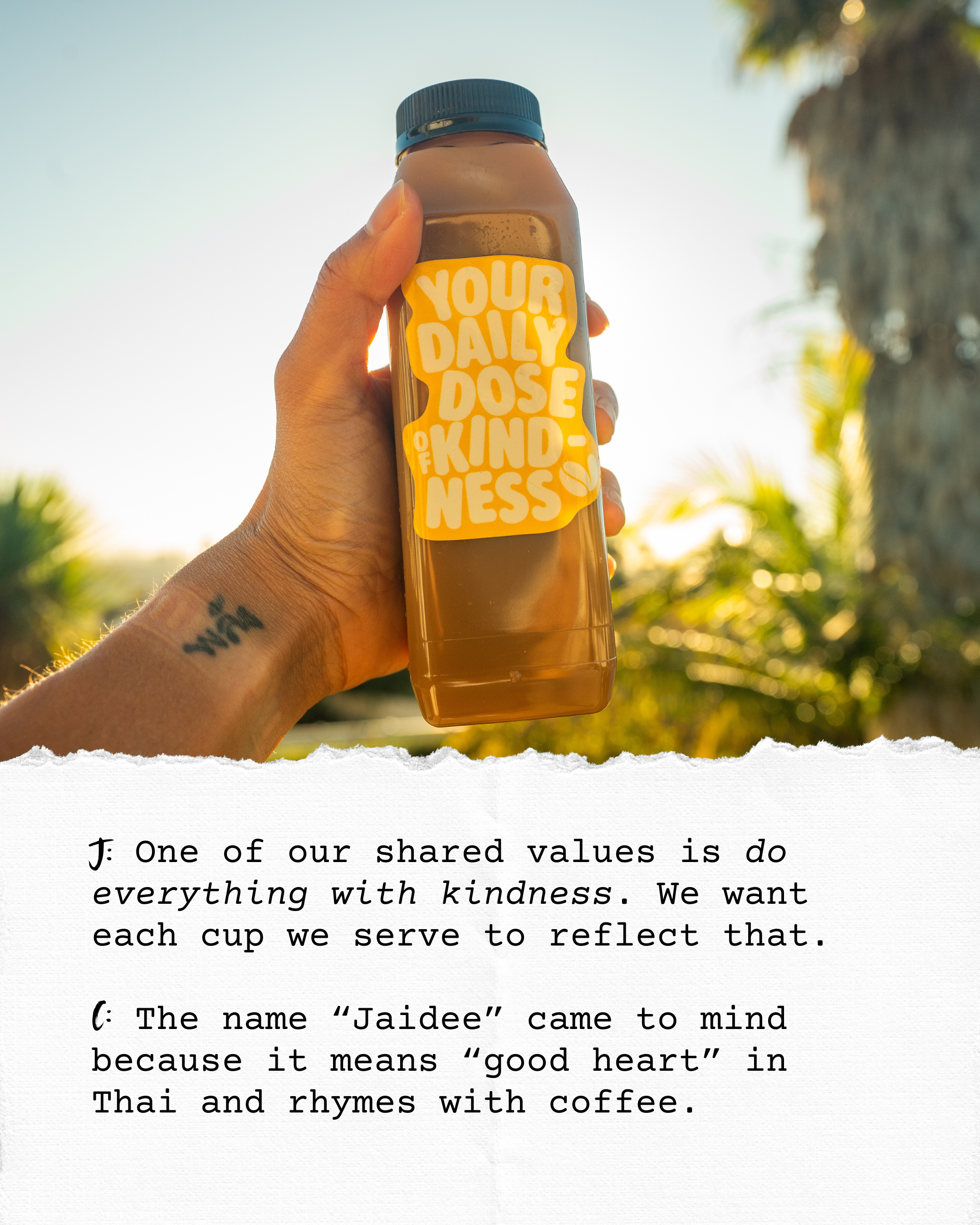 A hand holds a brown plastic bottle with a black cap and a bright yellow label that reads "Your Daily Dose of Kindness" against a background of trees and sky with sunlight.