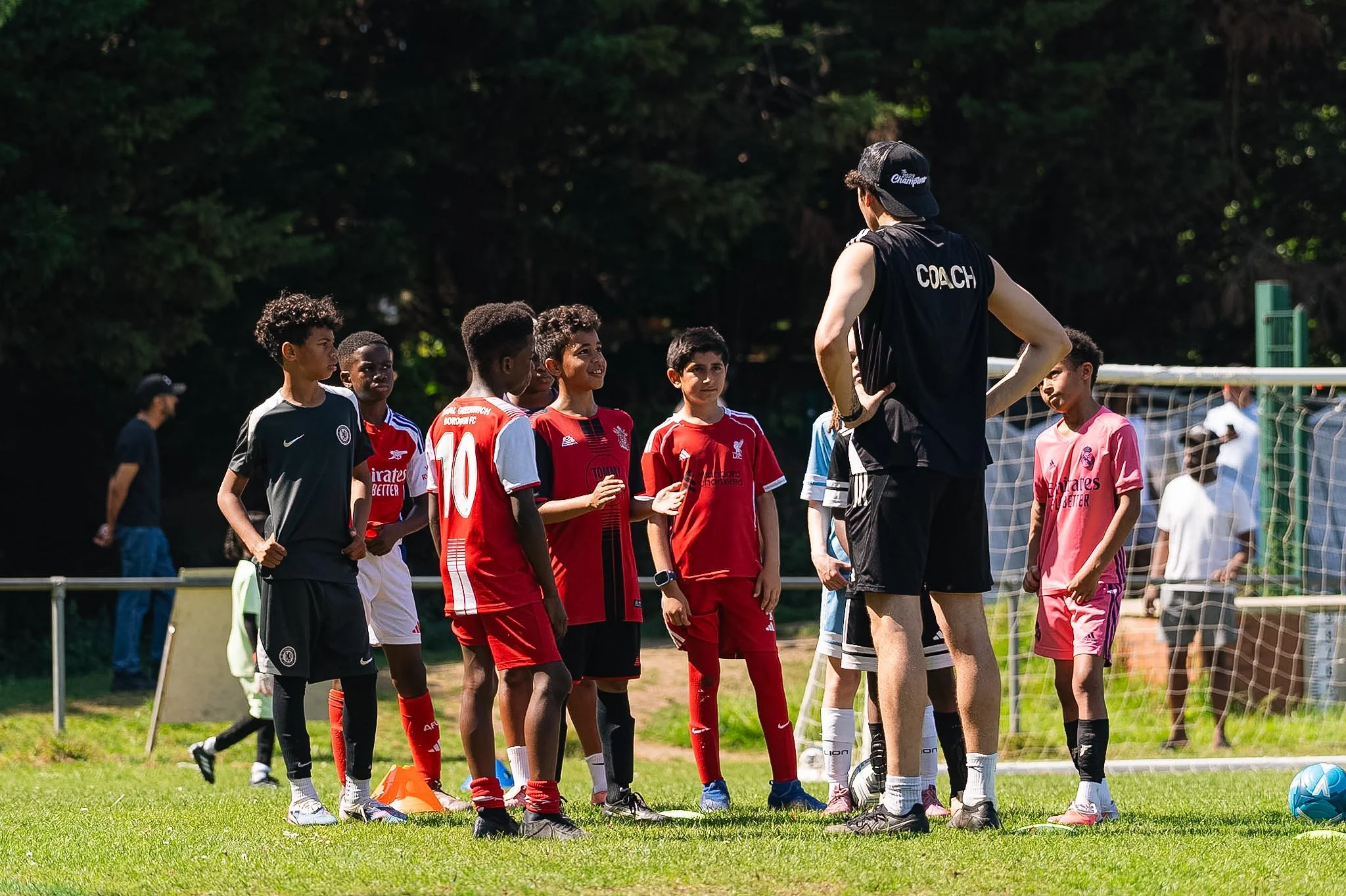 Young soccer players standing on a field listening to a coach during practice in the daytime.