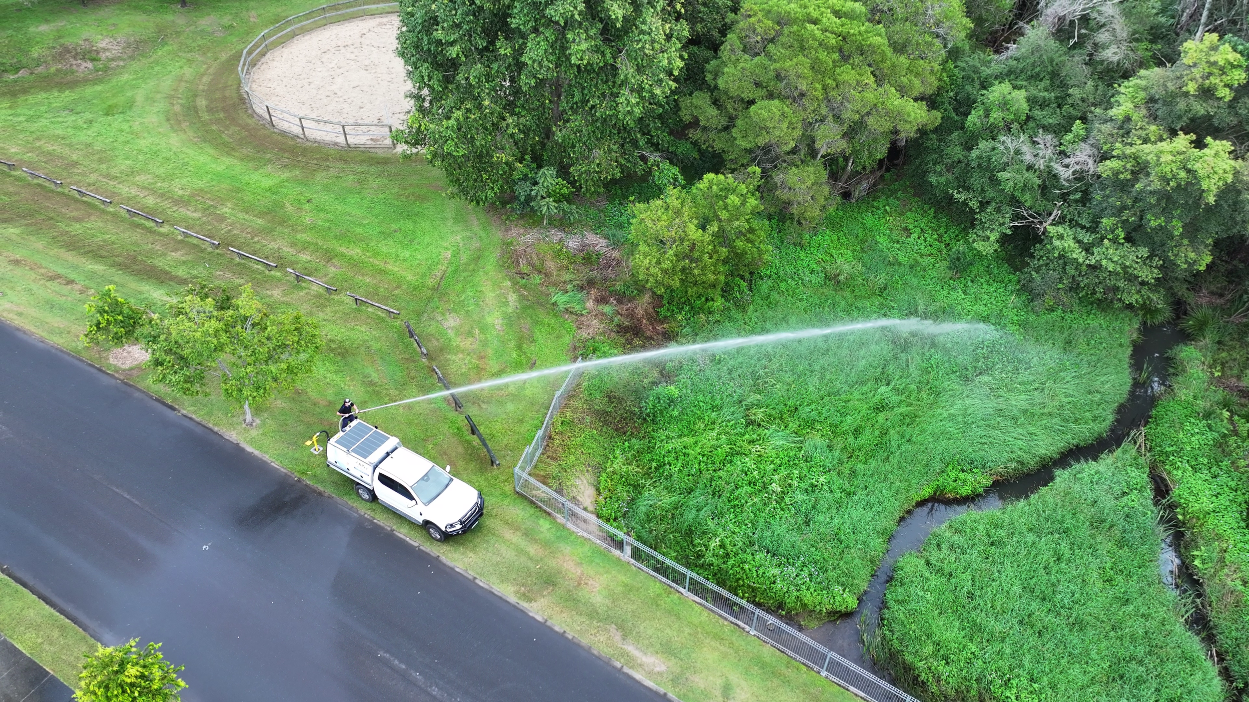 An aerial view of a person using a hose connected to a white utility truck spraying water at very high pressure demonstrating the firefighting capabilities of this compact electric pump.