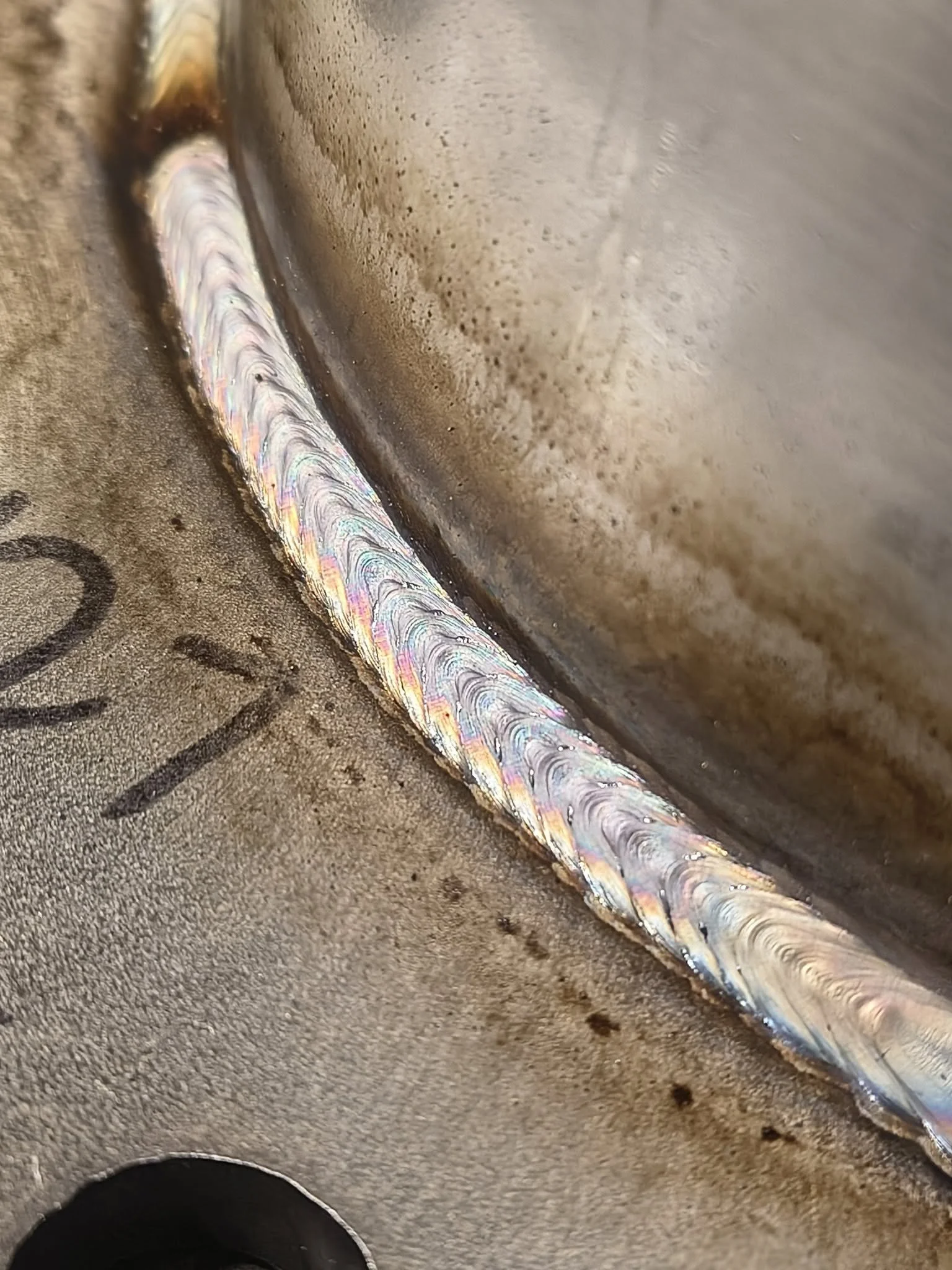 Close-up image of a weld on a metal surface showing colorful iridescent patterns.