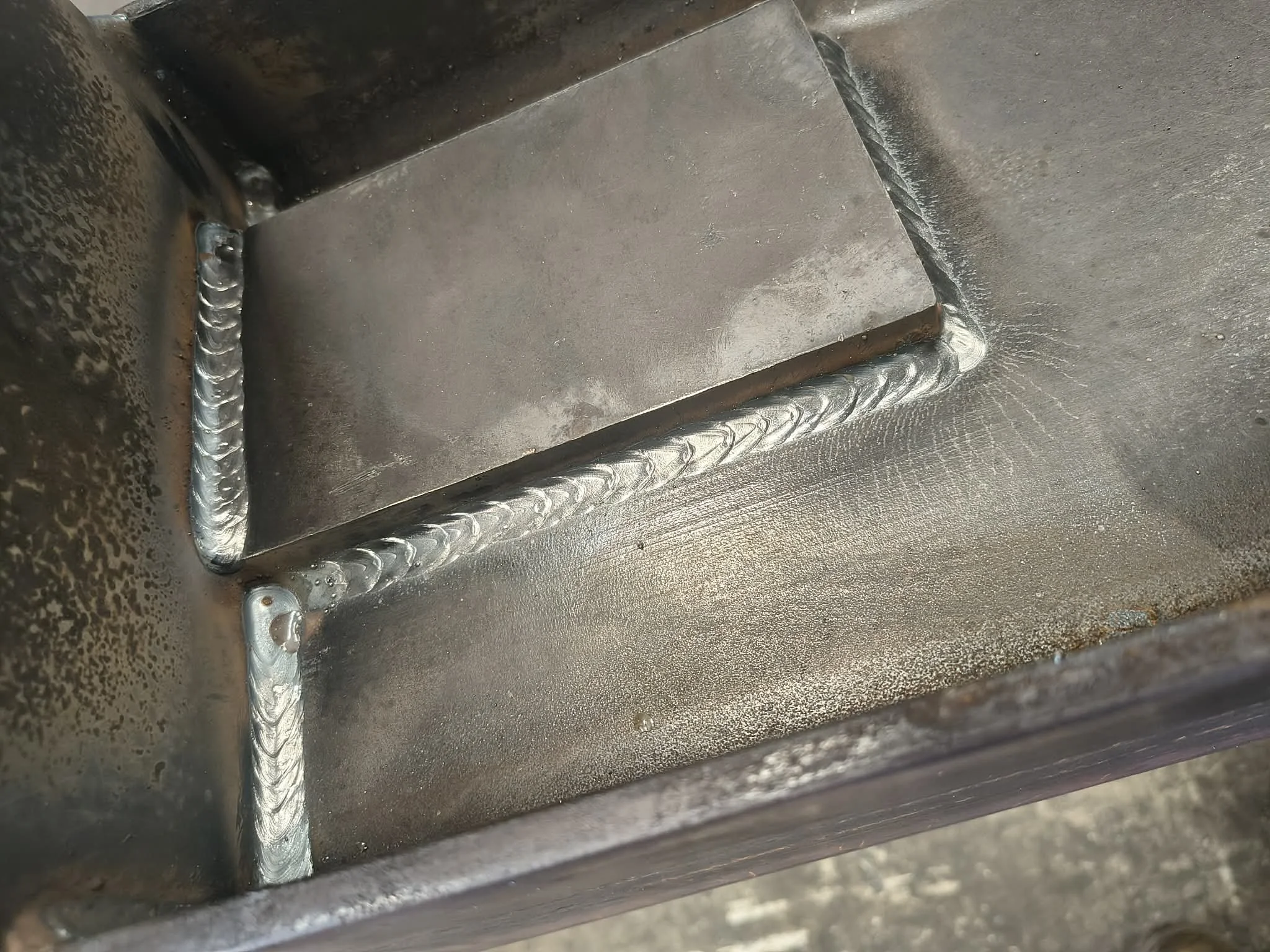 Close-up view of a welding joint on a metal structure, showing a well-executed weld bead along the corner of two metal pieces with a textured surface.