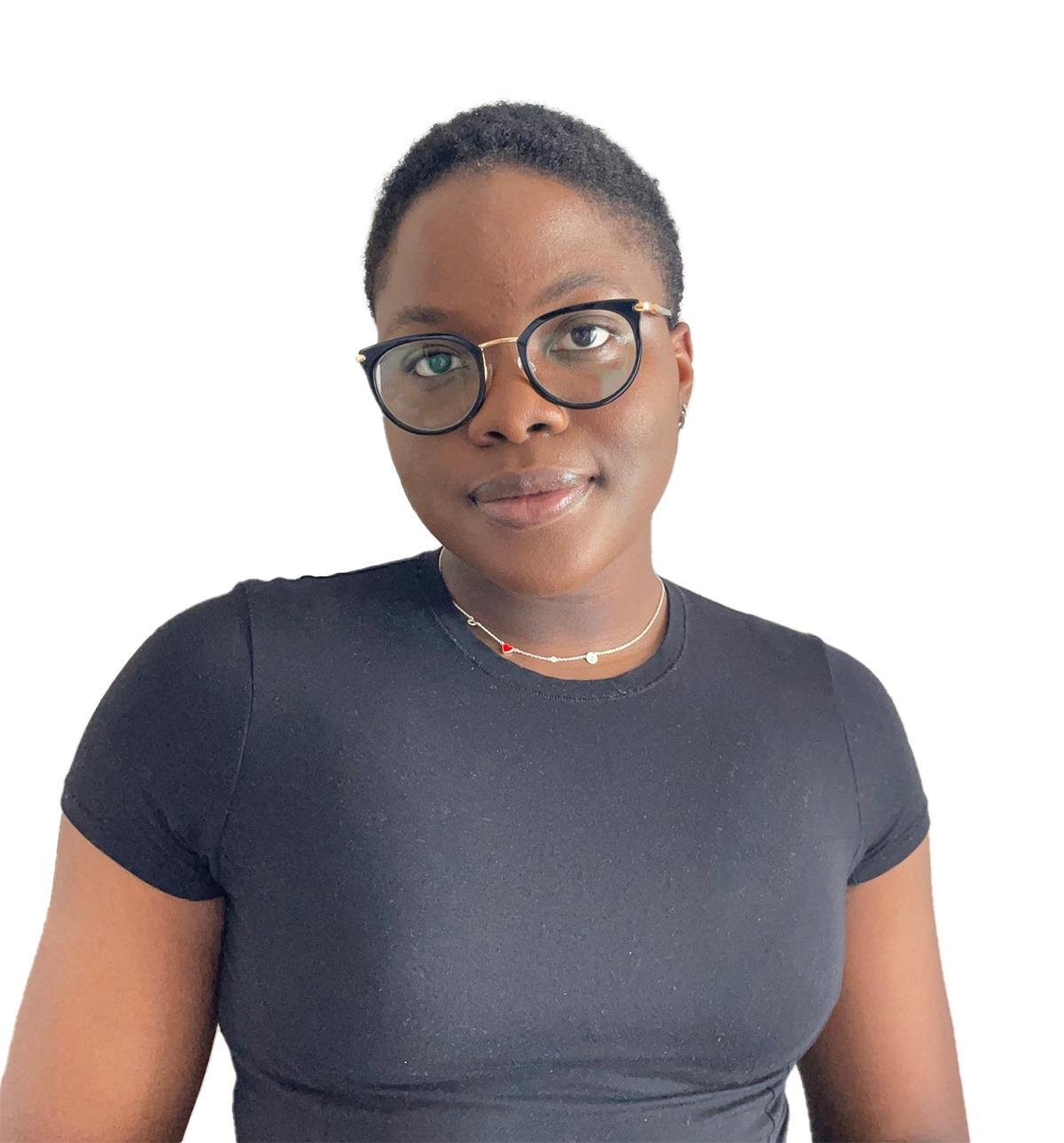 Portrait of a woman with short hair, glasses, wearing a black t-shirt and a delicate necklace, standing against a white background.