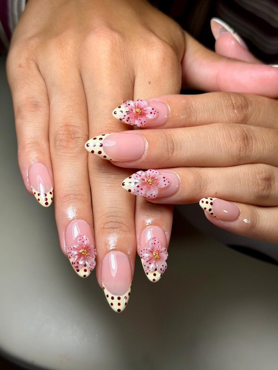 Close-up of hands with manicured nails featuring pink flowers, polka dots, and glitter accents.