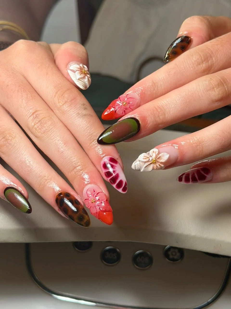 Close-up of hands with intricately designed floral and animal print nails in various colors.