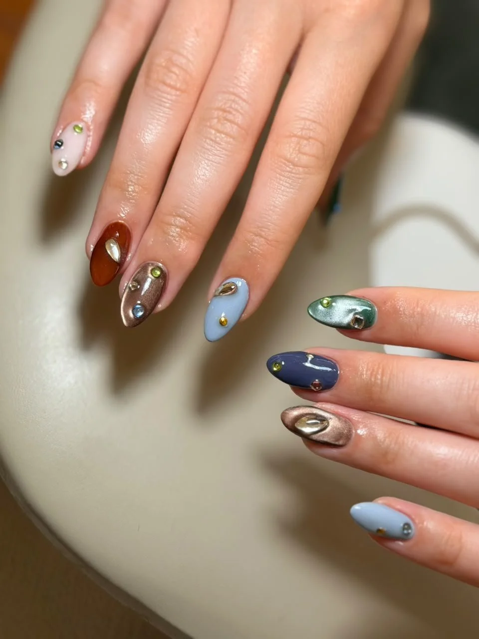 Close-up of hands with colorful, decorated nails resting on a white surface.