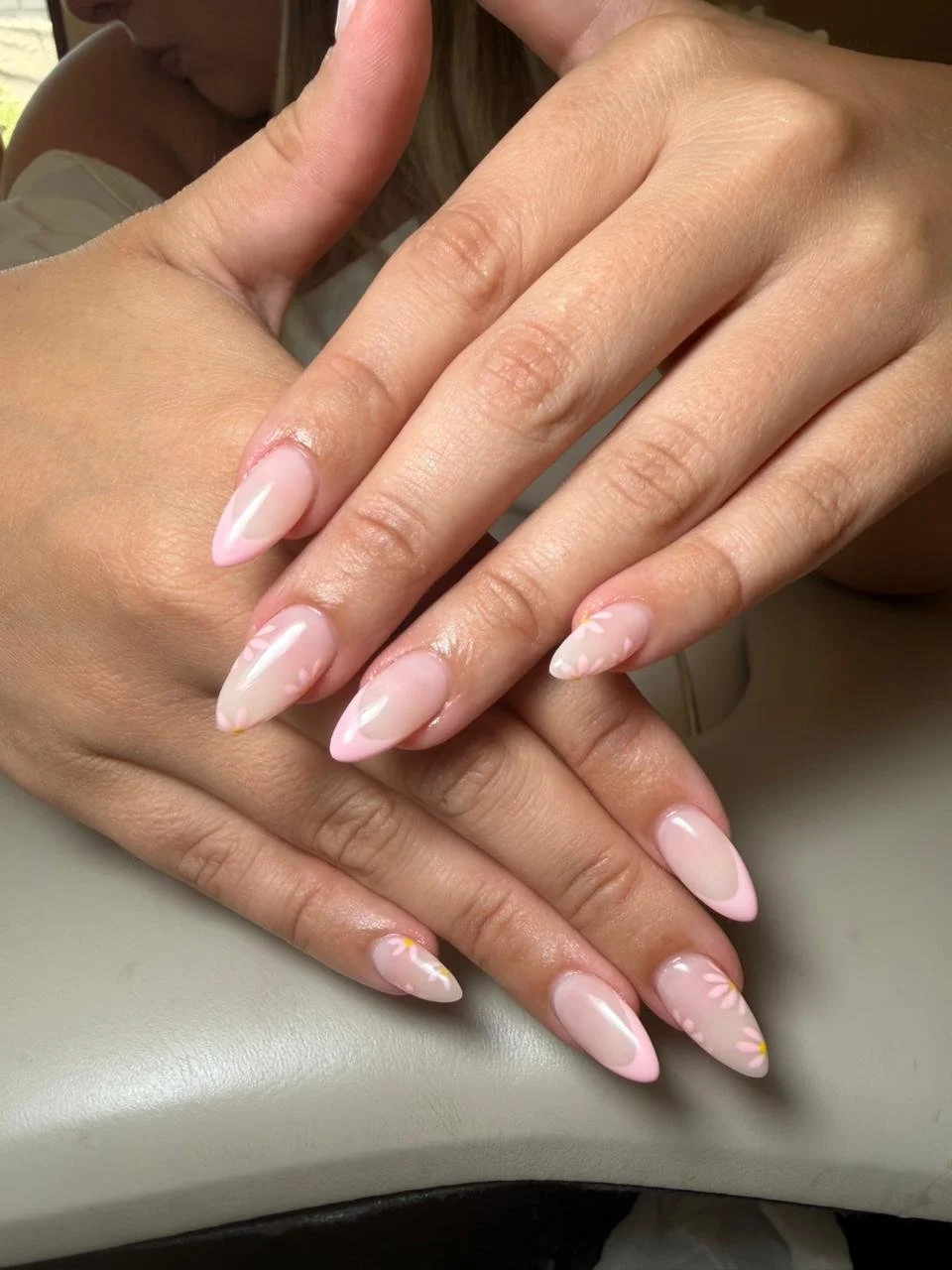 Close-up of a woman's hands with manicured nails painted in pink and white with floral designs.