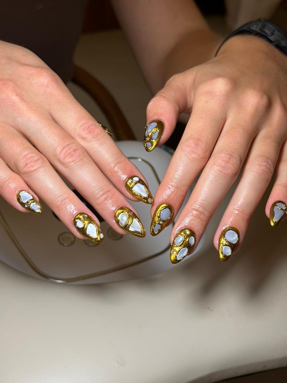 Hands with gold and white gel manicured nails resting on a table.