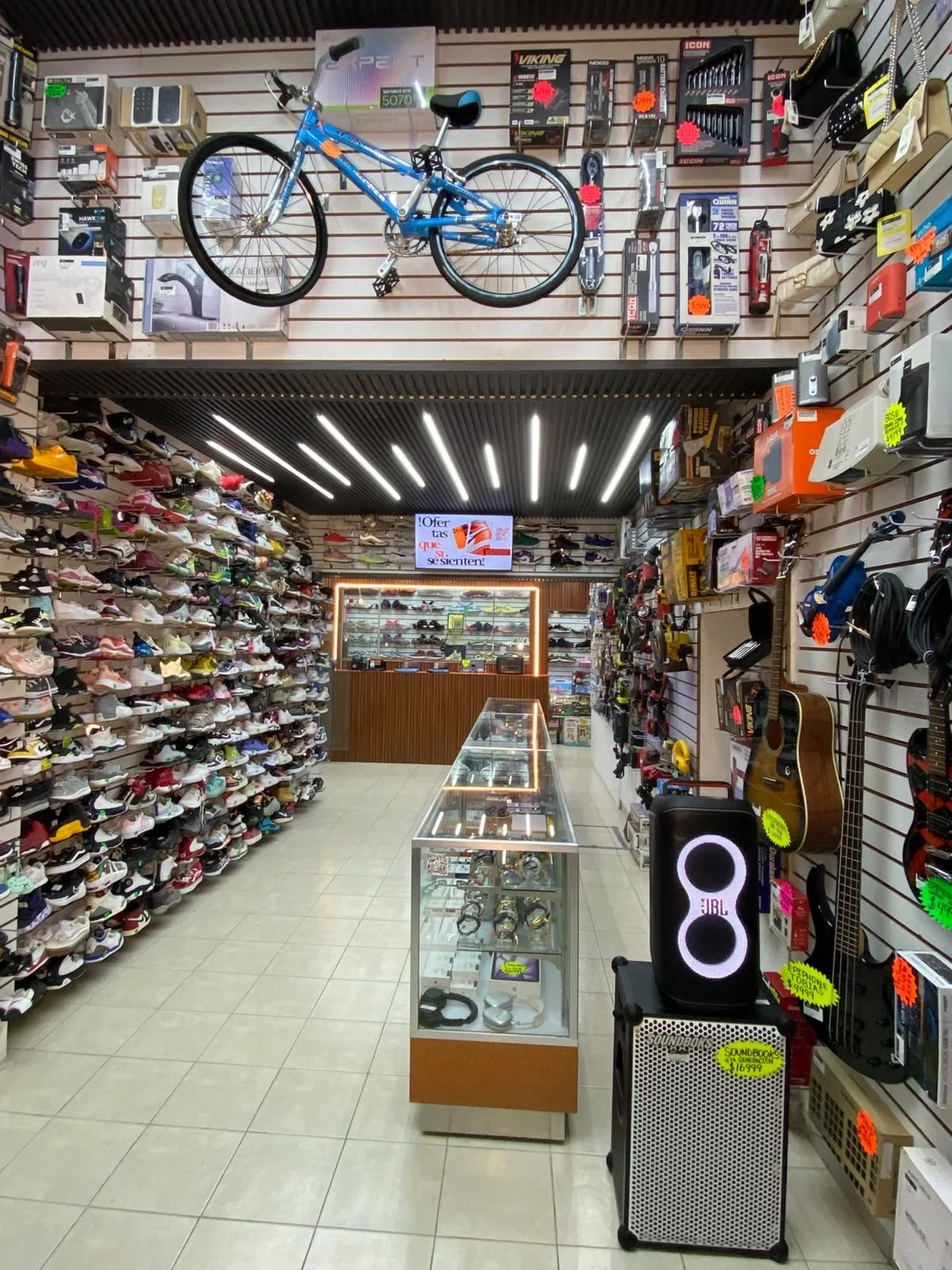 Casa de Empeño en San Pablo Tienda de artículos variados, con muchas calzado en la pared izquierda, ropa y accesorios en las paredes laterales, y vitrinas con productos en el centro. En la parte superior, hay una bicicleta azul montada en la pared.