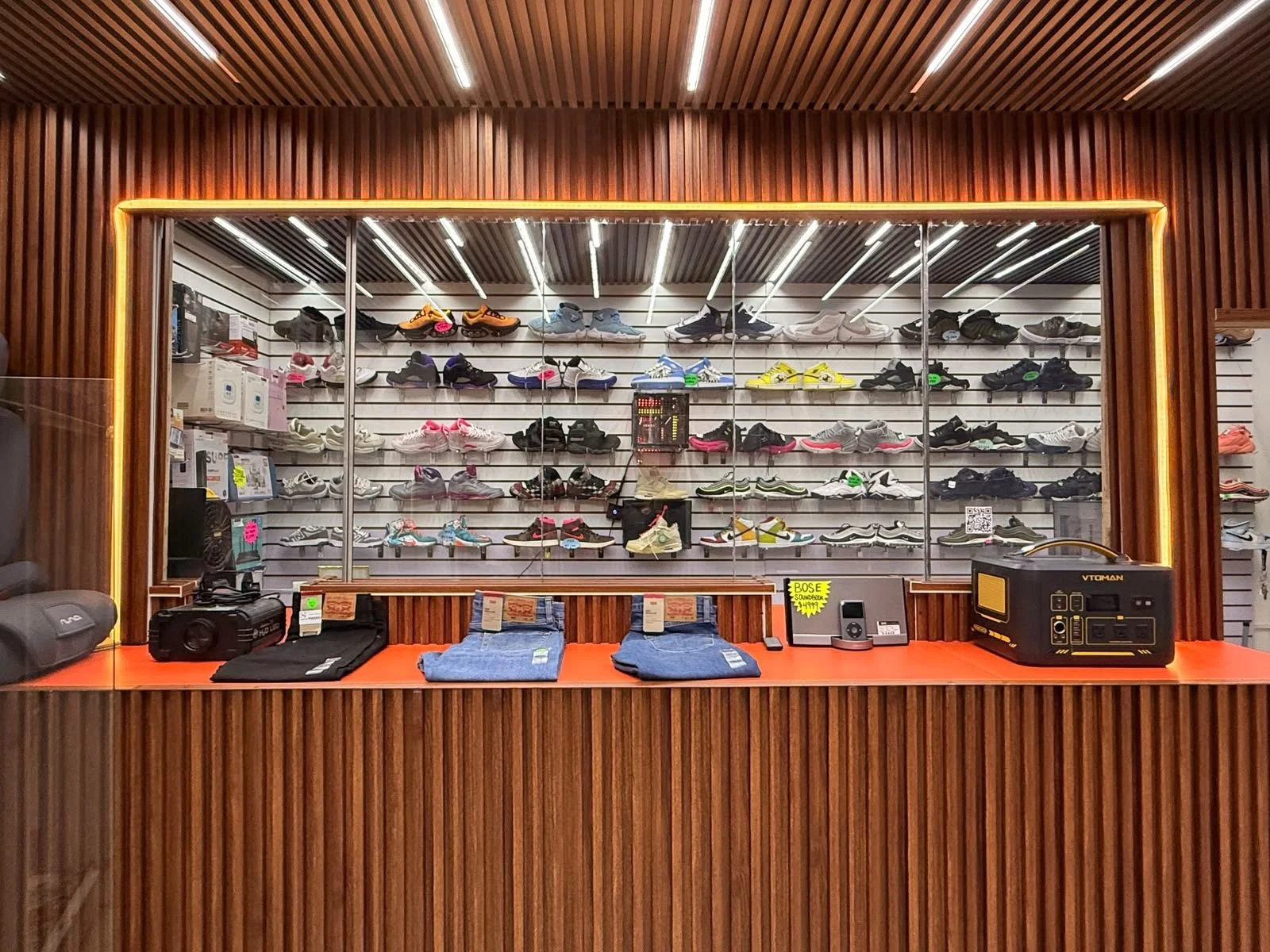 Casa de Empeño en San Pablo del Monte Tlaxcala Mostrador de tienda con zapatos deportivos en exhibición en una pared de fondo de madera con iluminación LED, y artículos como pantalones y equipo de audio en el mostrador.