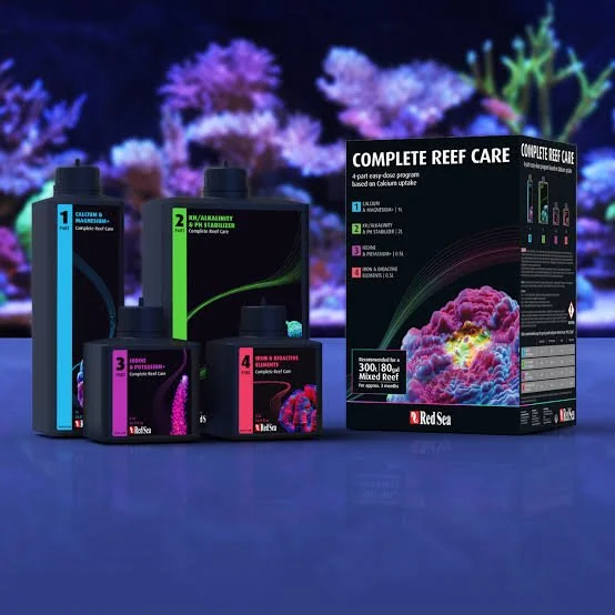 Aquarium care products in front of an illuminated reef tank, including bottles numbered 1 to 4 and a box labeled 'Complete Reef Care' with coral images.
