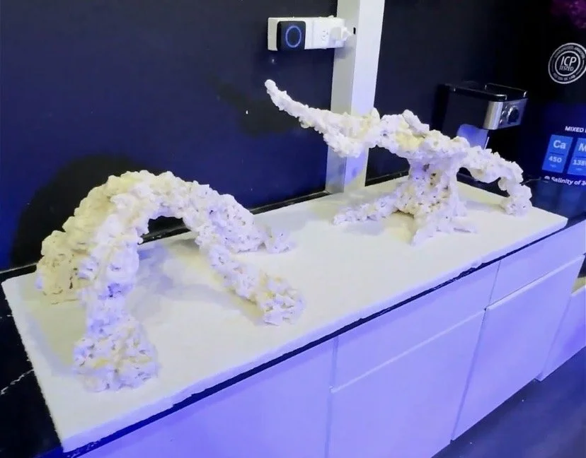 Foam sculptures resembling bridge structures on a white table, with a dark wall and electronic devices in the background.
