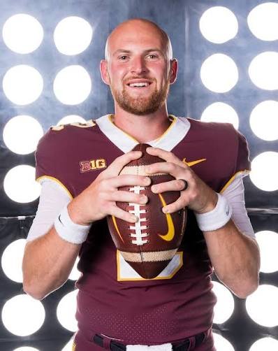 A football player in a maroon and white uniform holding an American football against a backdrop of illuminated circles.