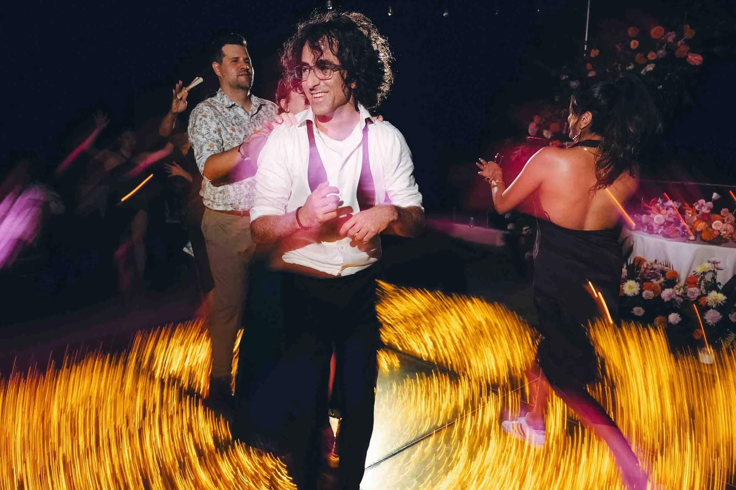 Person with curly black hair and glasses dancing the night away at a wedding party.