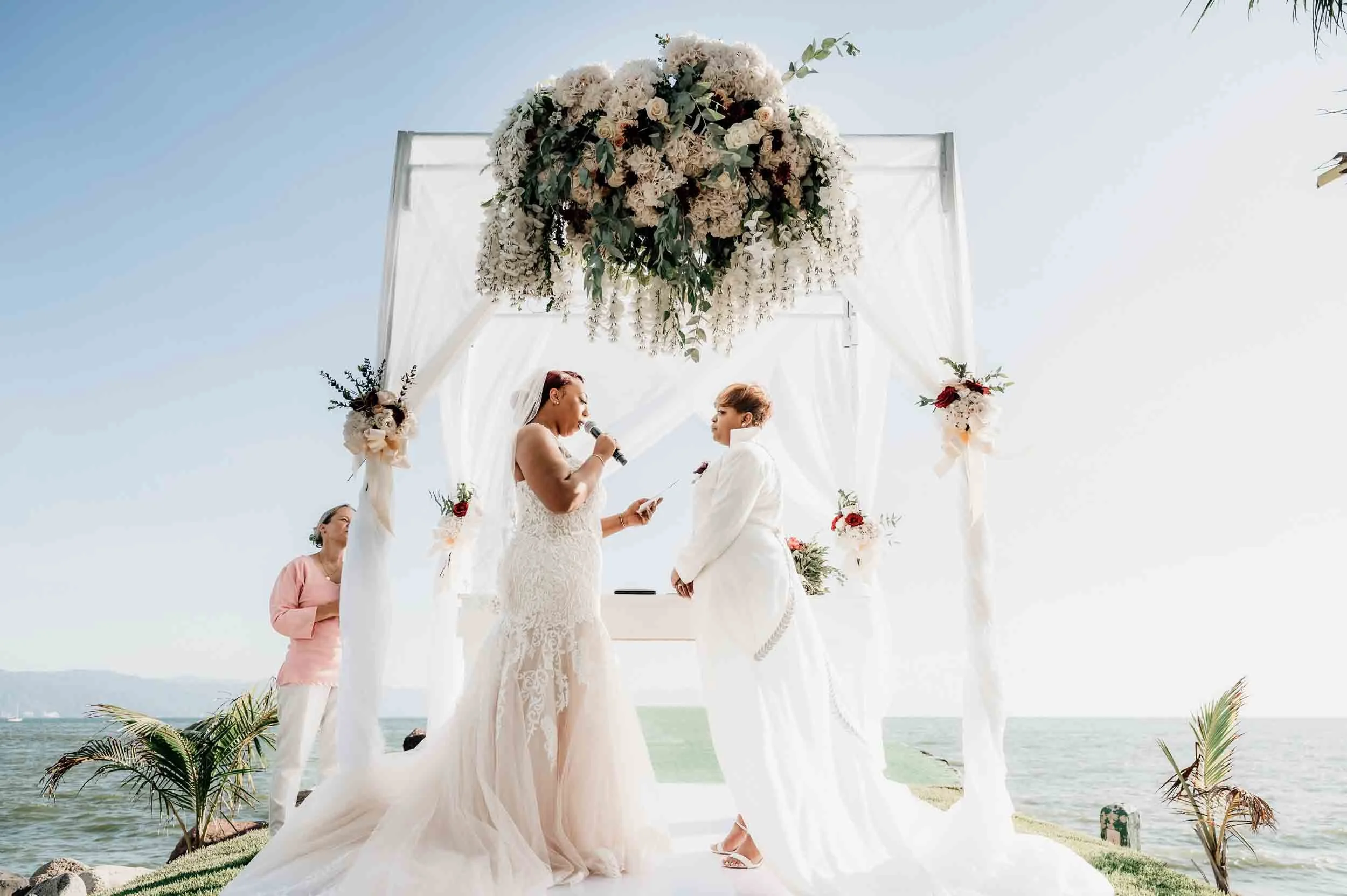 Lesbian brides during their vow exchange on their wedding day with a beach backdrop at the Marriott Resort in Puerto Vallarta
