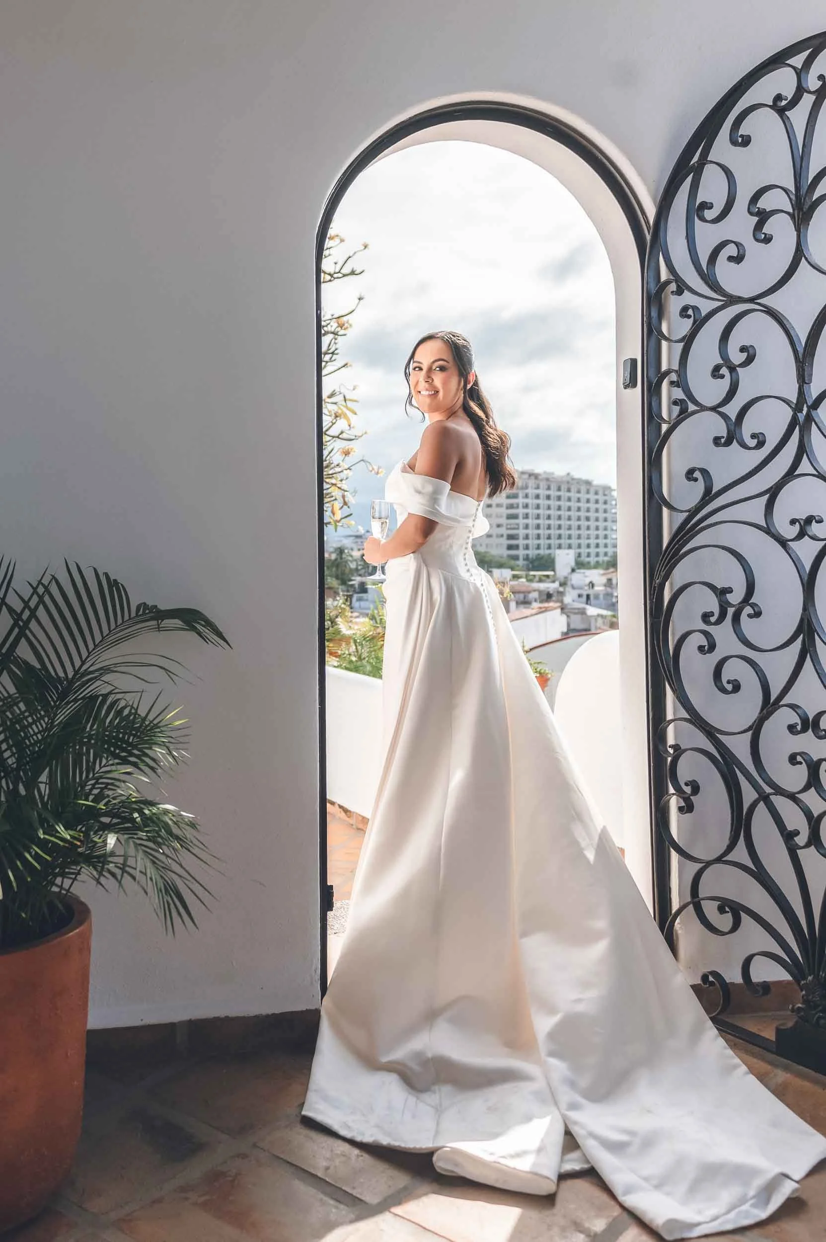 Bride looking back framed under an arc and an iron door, her dress has a long train.