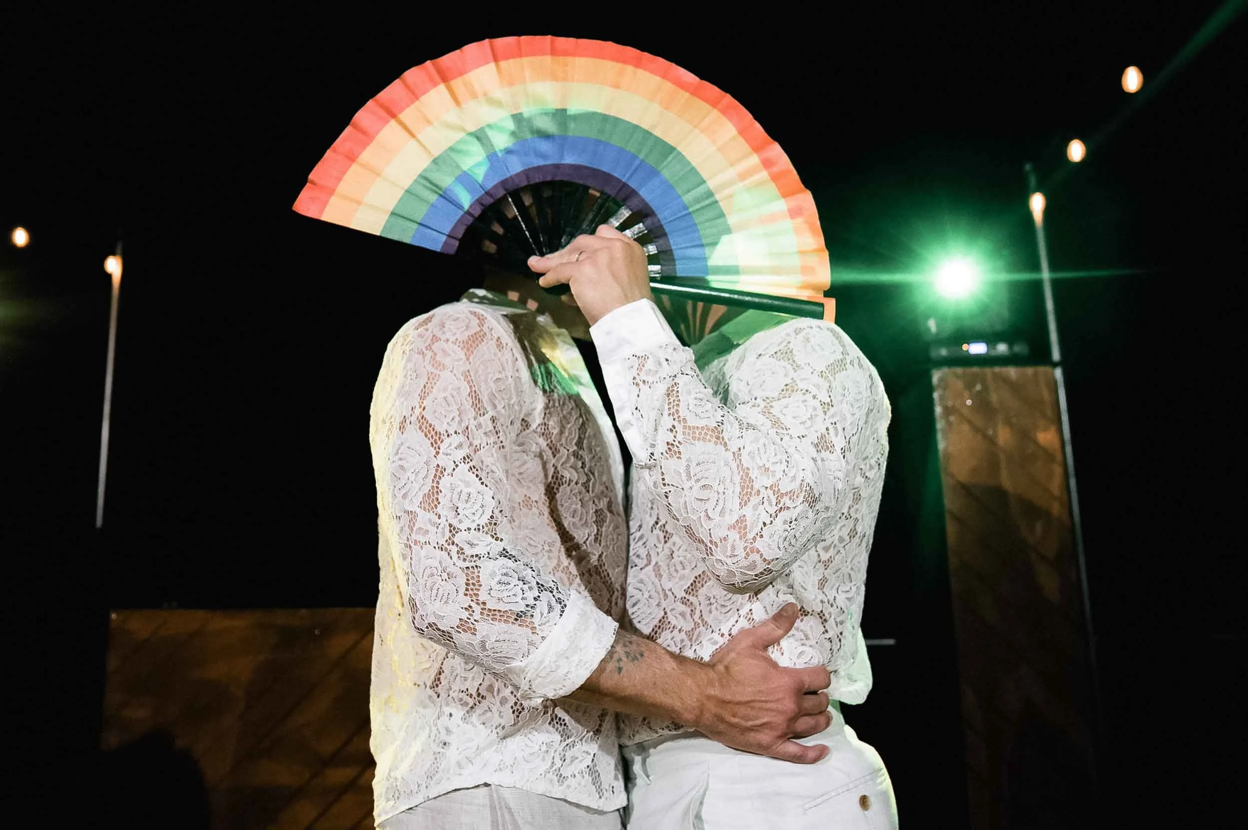 Gay couple kissing behind a rainbow fan during the reception of their destination wedding at the Grand Miramar luxury resort in Puerto Vallarta